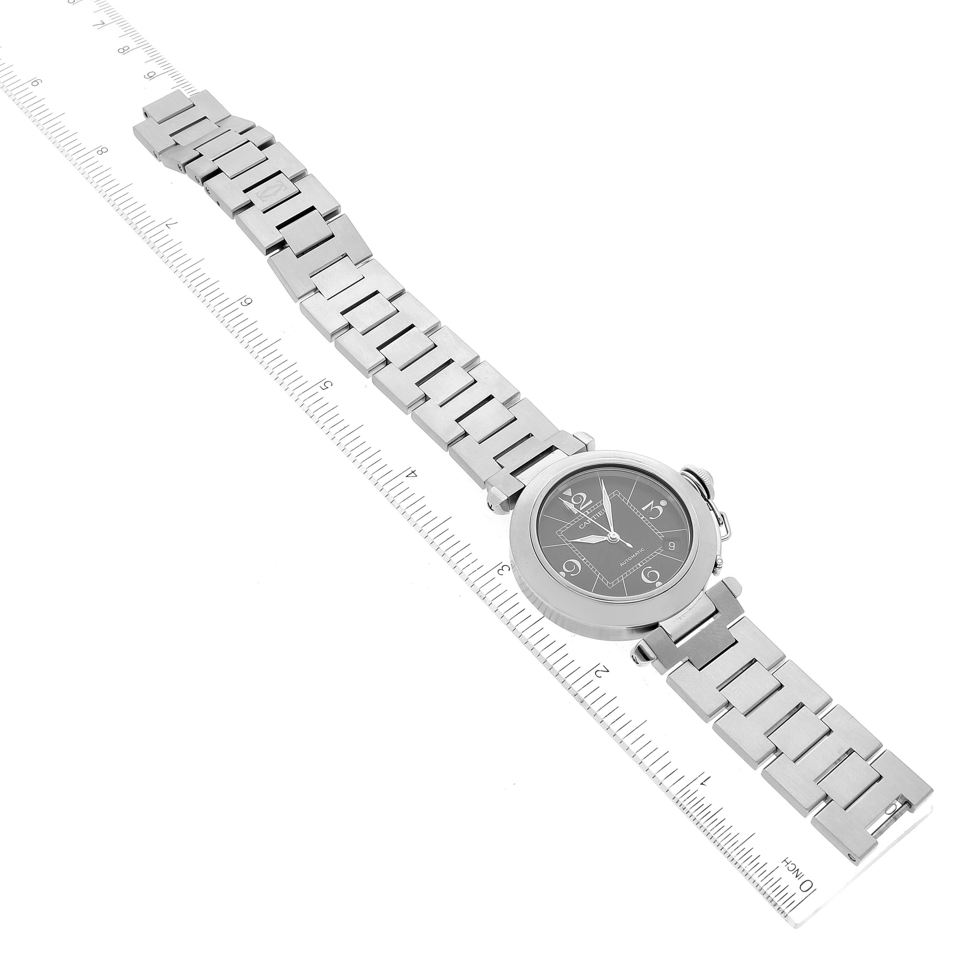 The image shows an overhead view of a Cartier Pasha W31076M7 Women's Stainless Steel Black Dial W31076M7 Women's Stainless Steel Black Dial watch, displaying its face and metal bracelet alongside a ruler for scale.