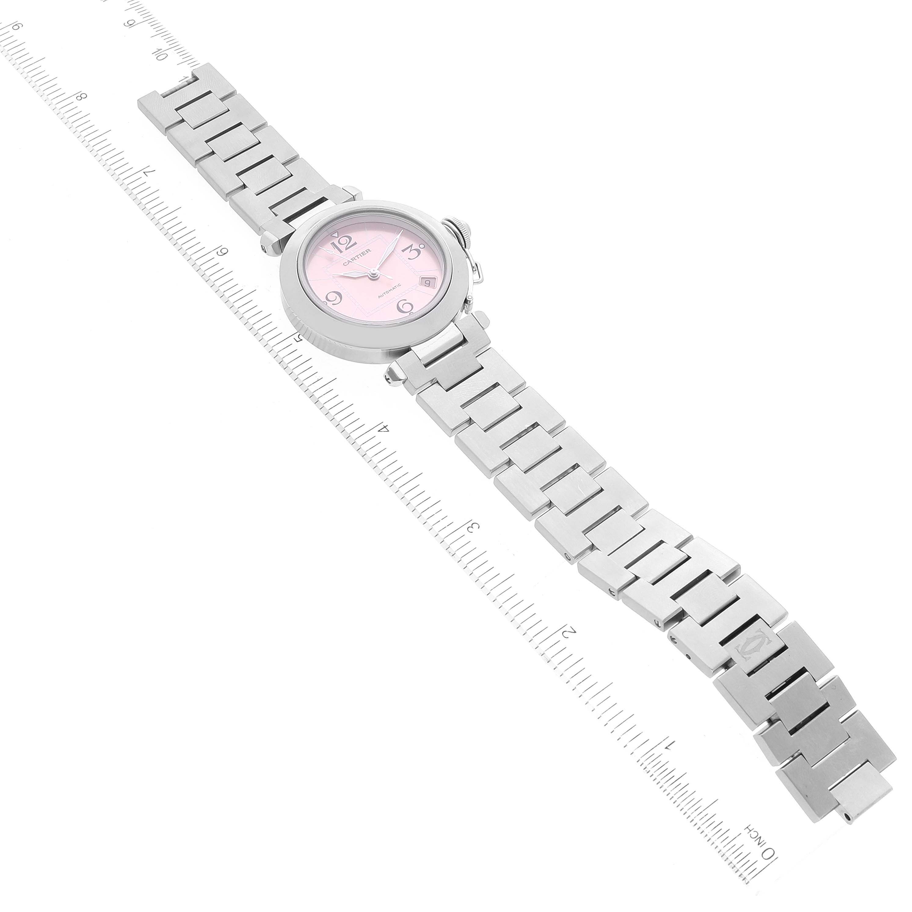 The image shows a top view of the Cartier Pasha W31075M7 Women's Stainless Steel Pink Dial W31075M7 Women's Stainless Steel Pink Dial watch, highlighting its face, bezel, and metal bracelet alongside a ruler for scale.