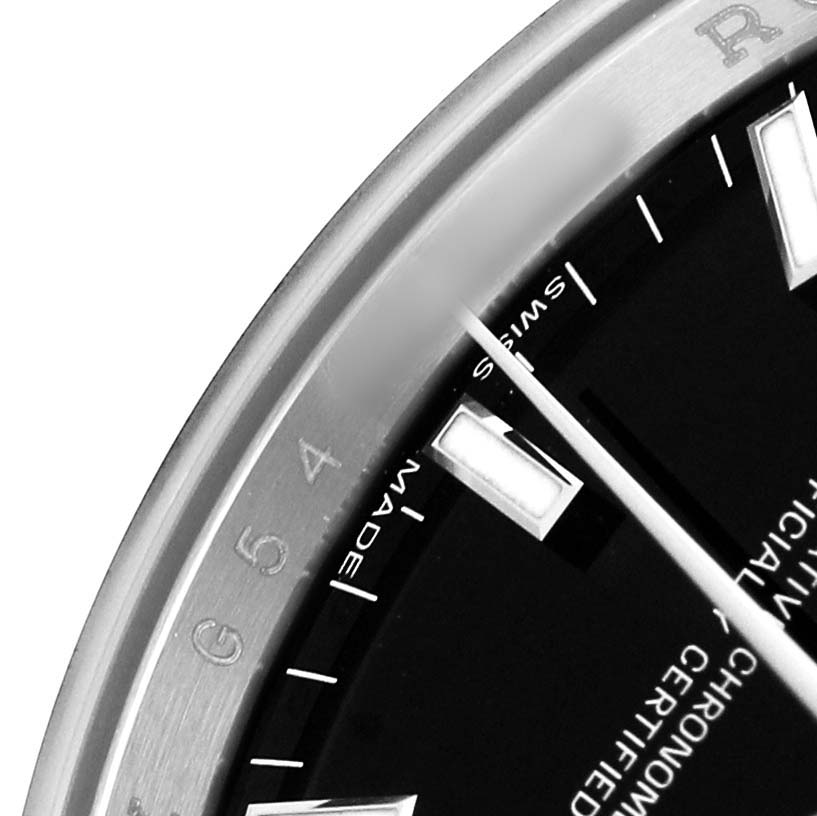 The image shows a detailed close-up of the dial and bezel of a Rolex Date 115200 Men's Stainless Steel Black Dial watch with visible indices and text.