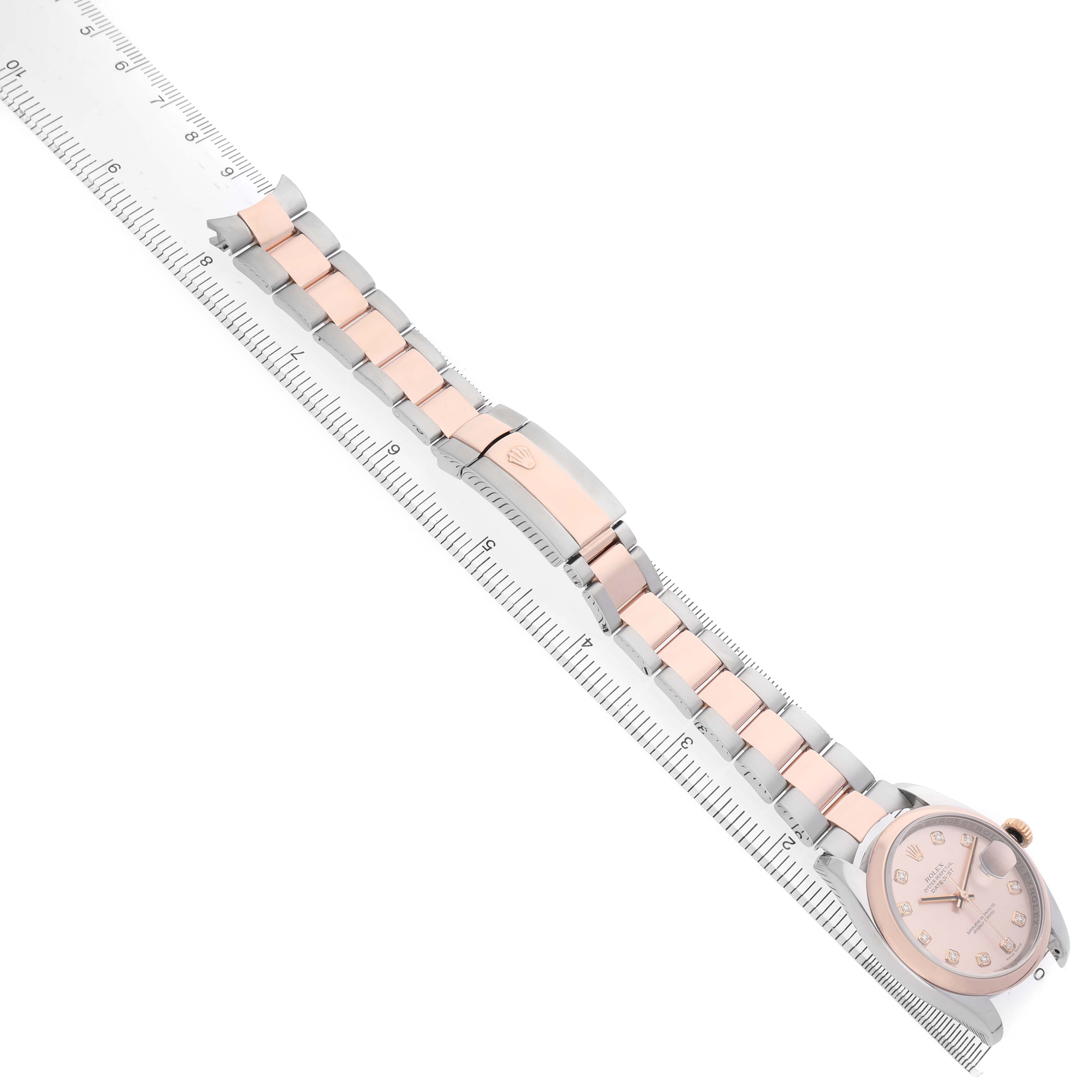 The image shows the Rolex Datejust 116201 Women's Stainless Steel Pink Dial watch from a top-down angle, featuring the face, bracelet, and clasp alongside a ruler.
