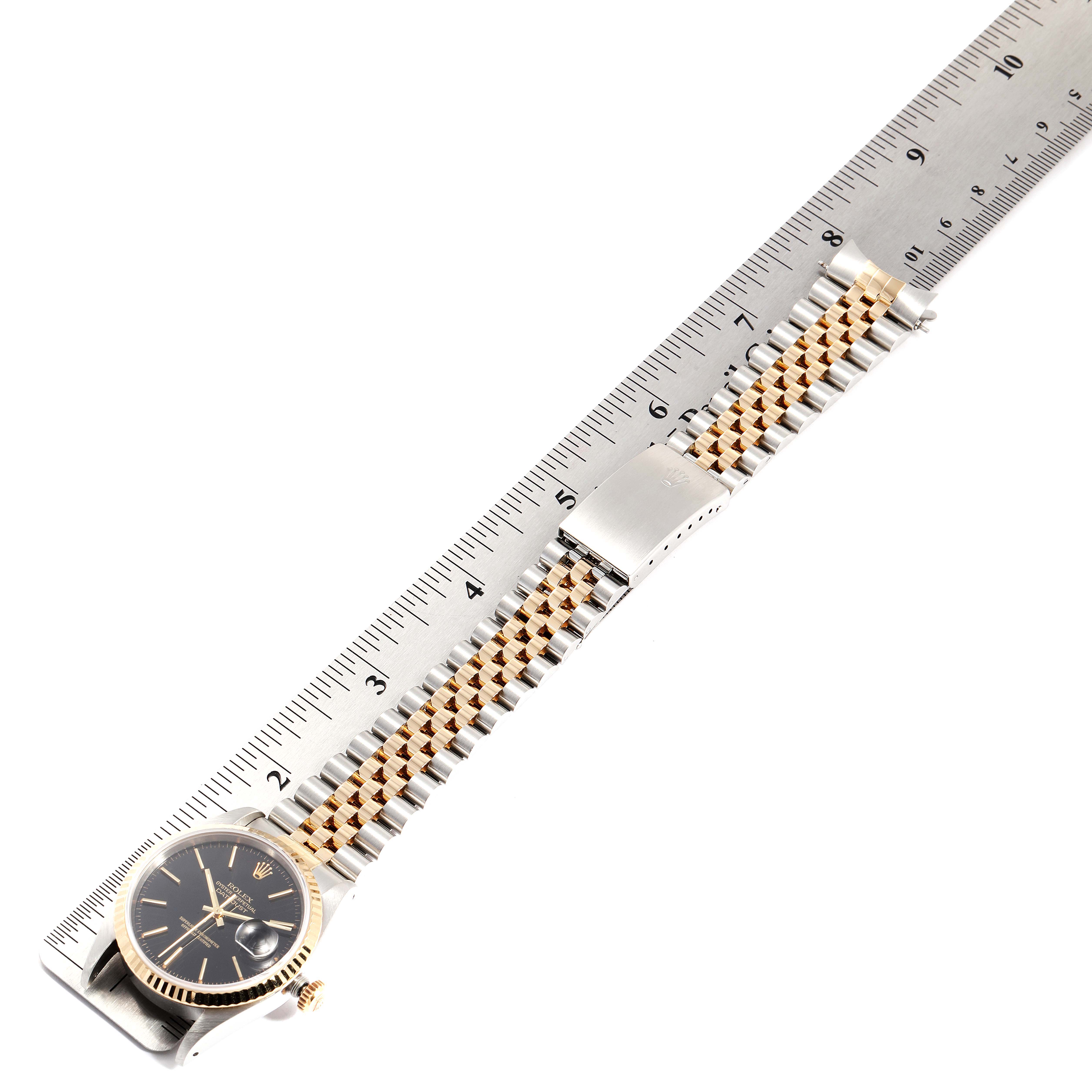 This image shows a Rolex Datejust 16233 Men's Steel and Gold (two tone) Black Dial 16233 Men's Steel and Gold (two tone) Black Dial watch lying flat with its full bracelet and clasp visible, aligned alongside a ruler.
