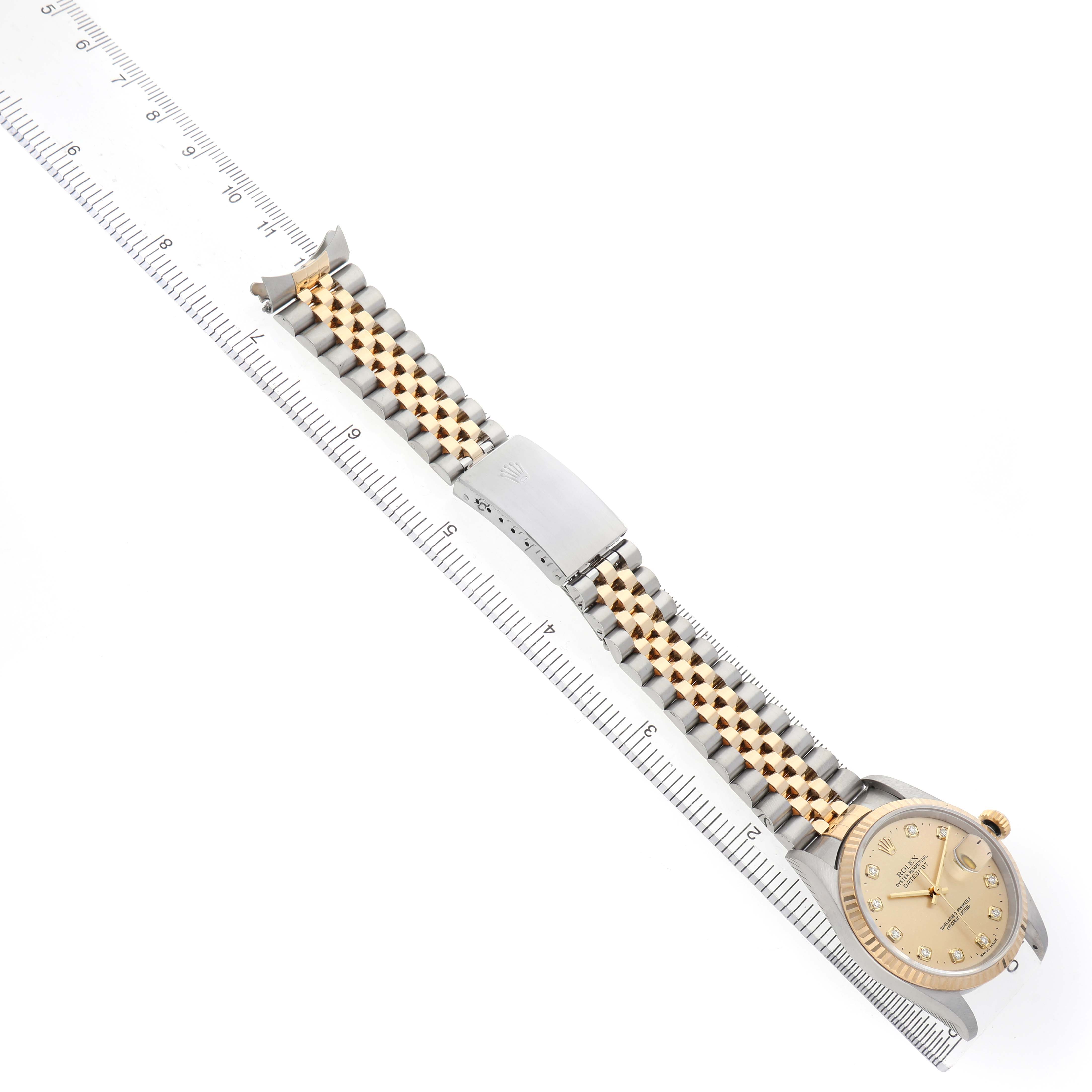 The Rolex Datejust 116233 Men's Steel and Gold (two tone) Champagne Dial watch is displayed from an overhead angle, showing the bracelet, clasp, and face alongside a ruler for scale.