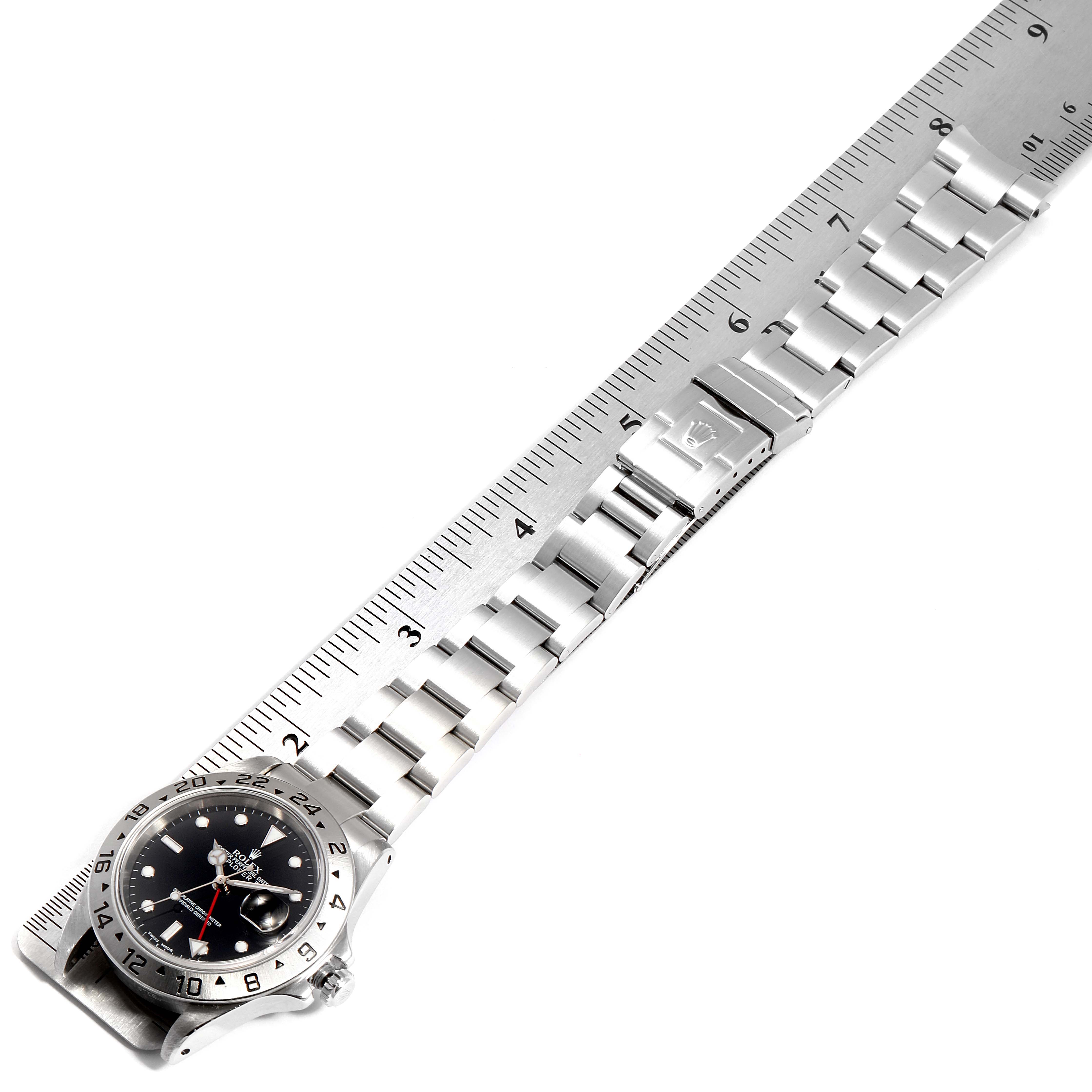 The image shows a Rolex Explorer 16570 Men
s Stainless Steel Black Dial 16570 Men
s Stainless Steel Black Dial watch, displaying its dial, metal bracelet, and clasp from a top-down angle alongside a ruler.