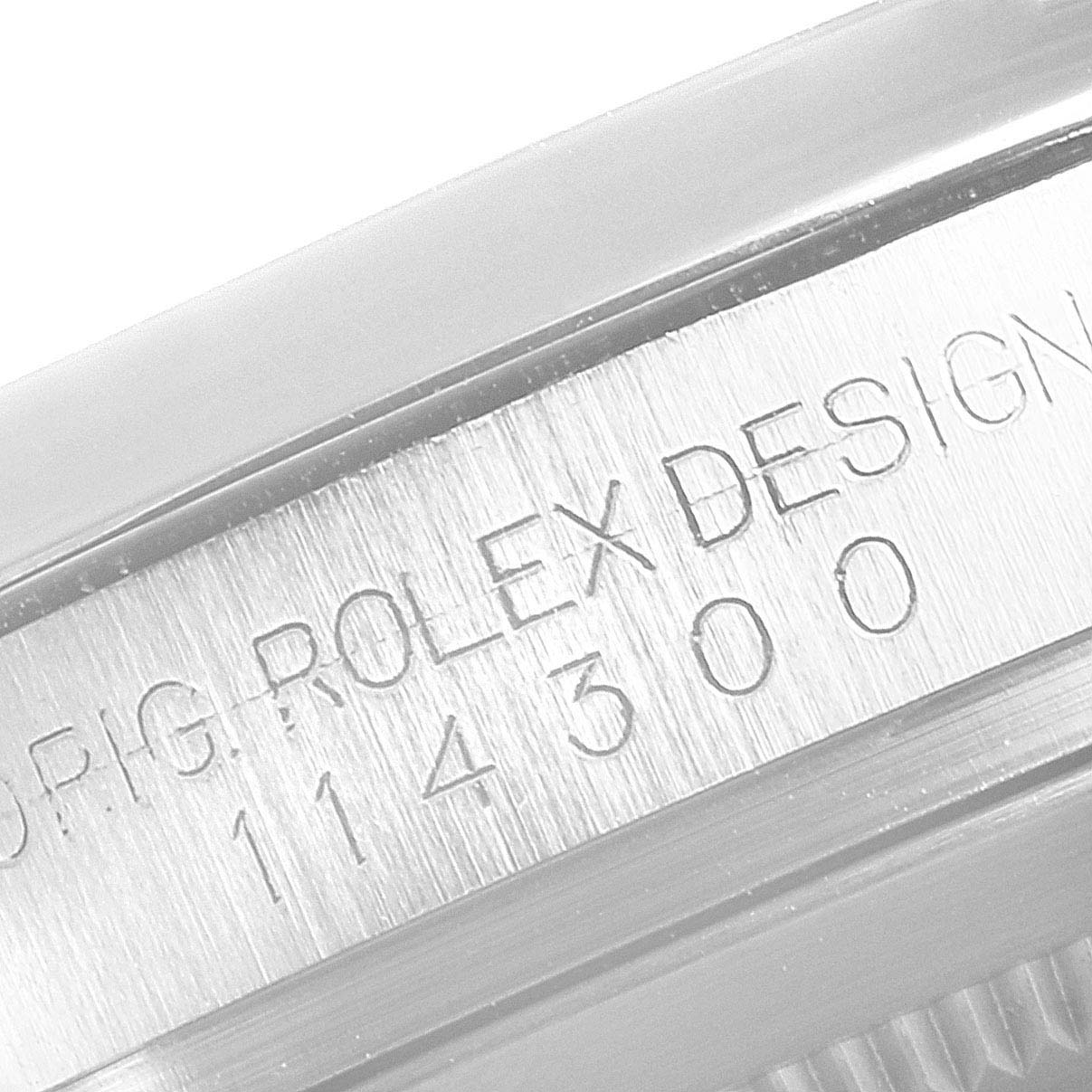 The image shows a close-up of the serial number engraving on the side of a Rolex Oyster Perpetual 114300 Men's Stainless Steel Black Dial 114300 Men's Stainless Steel Black Dial watch case.