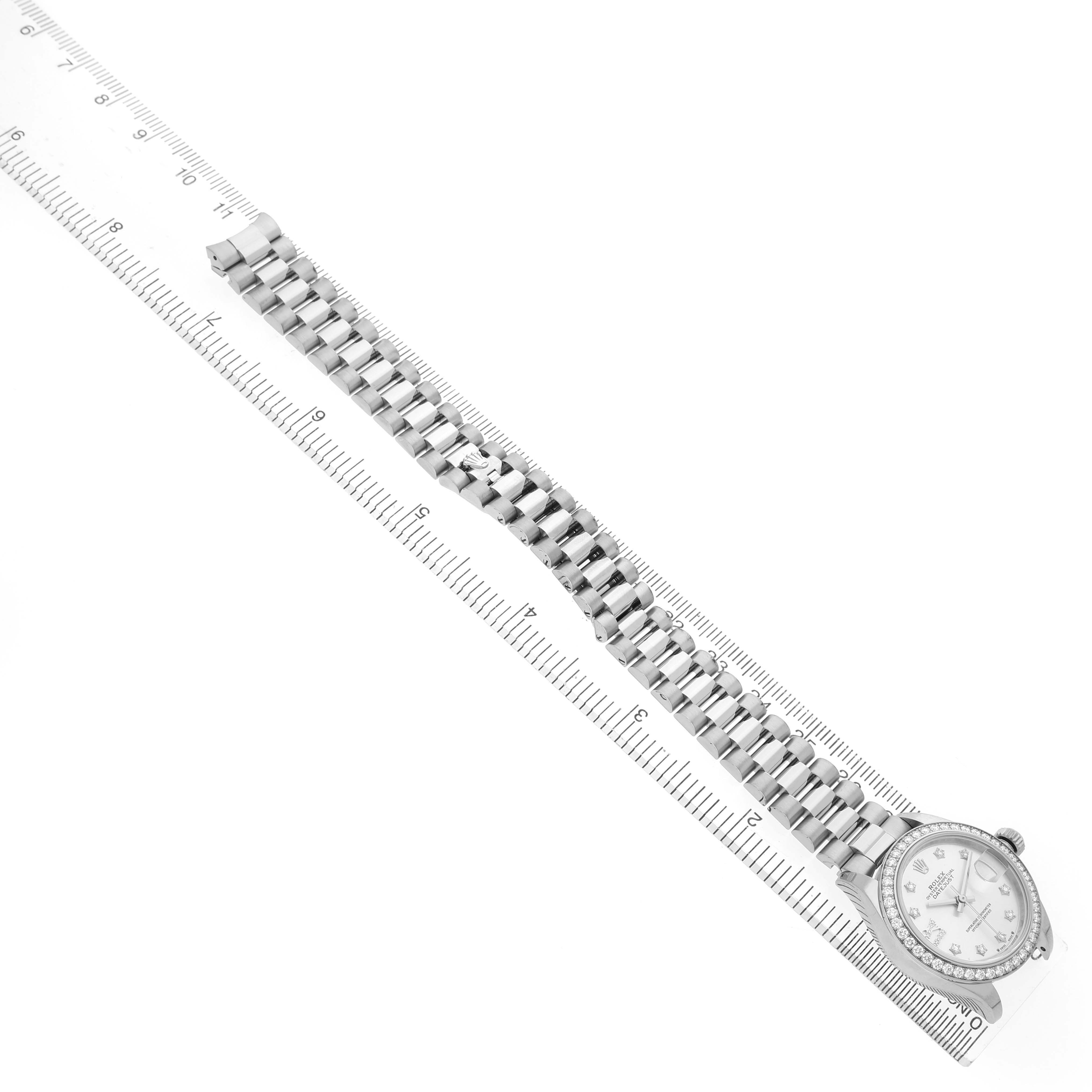 The Rolex President 279139 Women's White Gold Silver Dial model watch is shown from a top-down angle, highlighting the full bracelet and face alongside a ruler for scale.