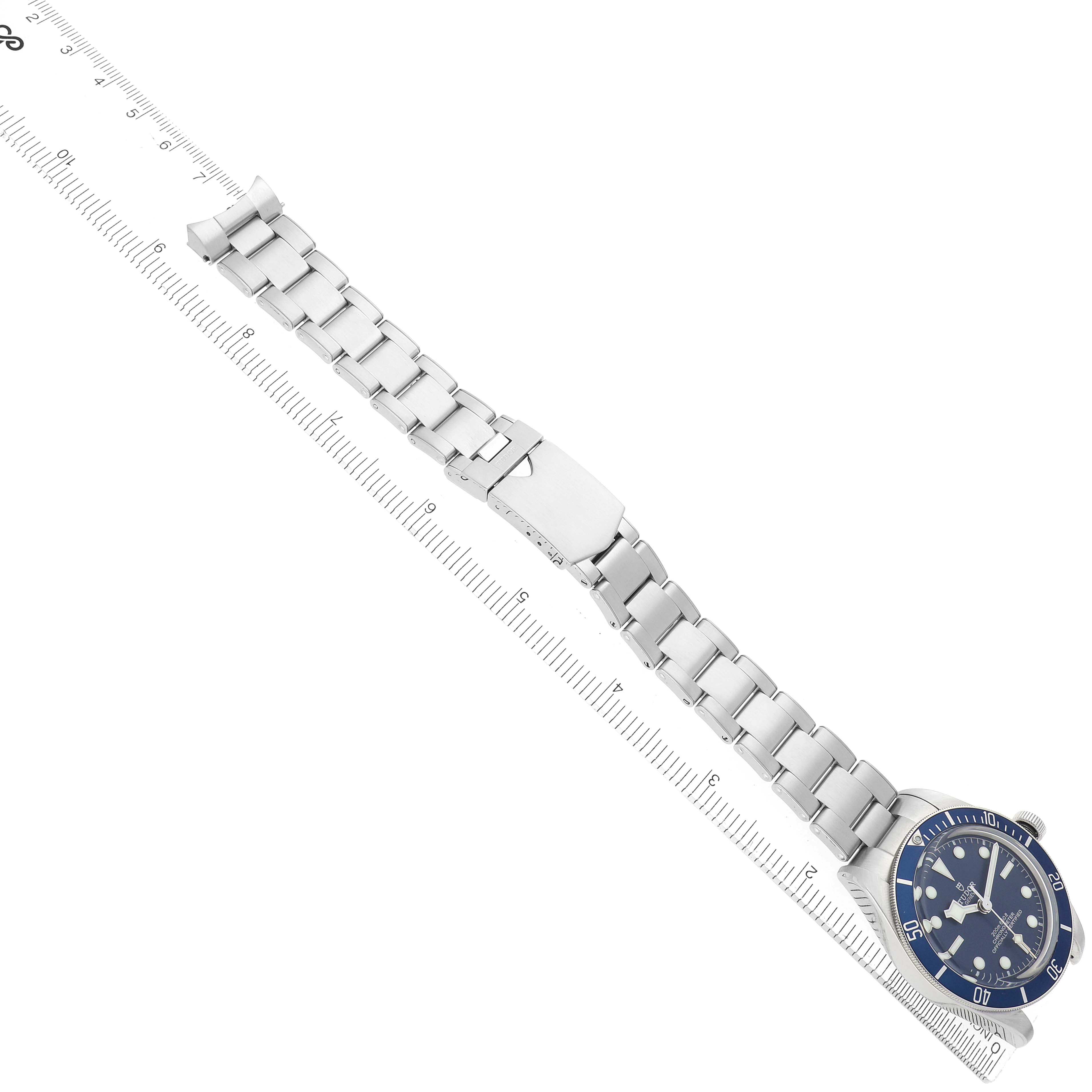 The Tudor Heritage Black Bay 79030B Men
s Stainless Steel Blue Dial watch is shown from a top angle, highlighting its bezel, face, and metal bracelet alongside a ruler.