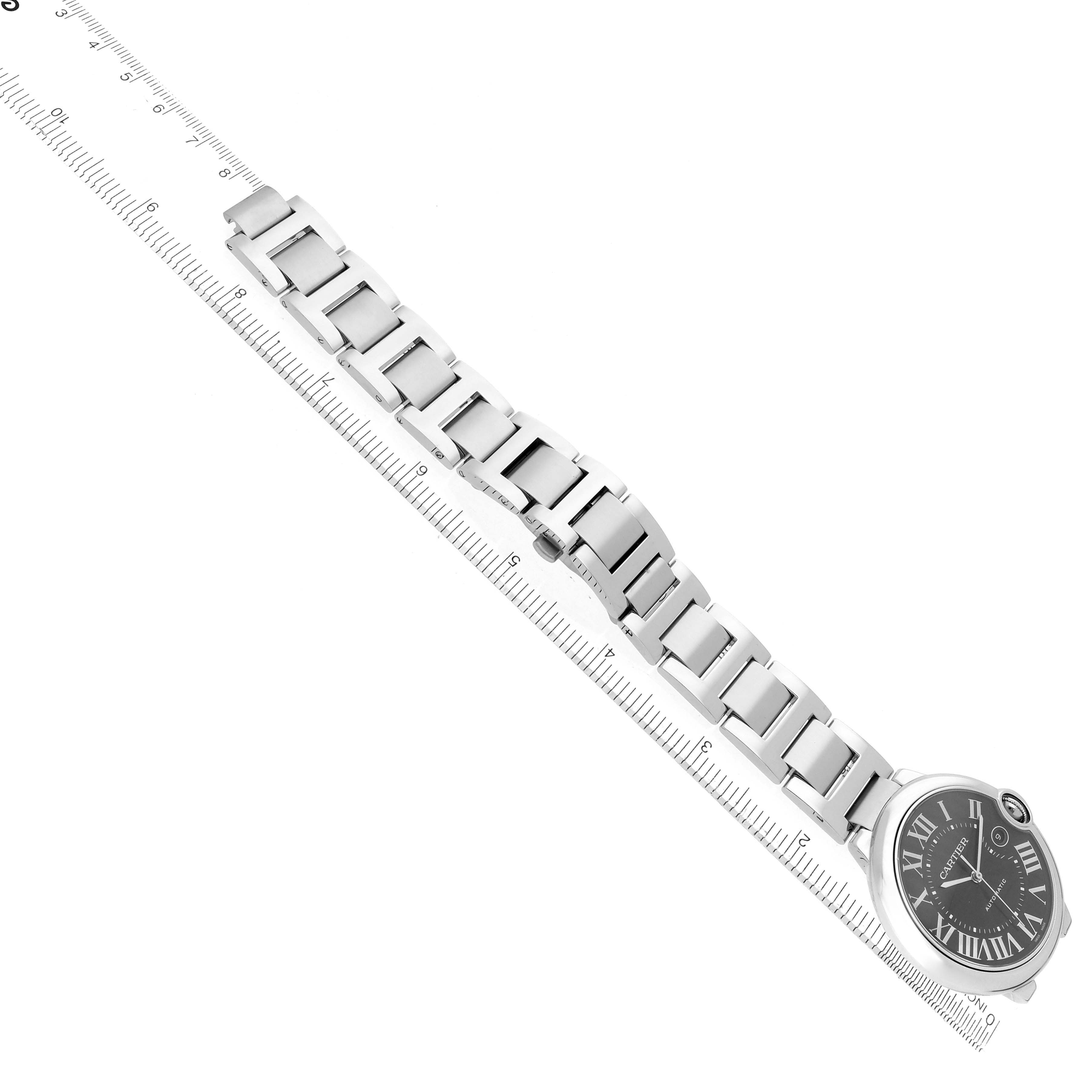 The Cartier Ballon Bleu W6920042 Men's Stainless Steel Black Dial watch is shown from a top-down angle, displaying its bracelet and face alongside a ruler for scale.