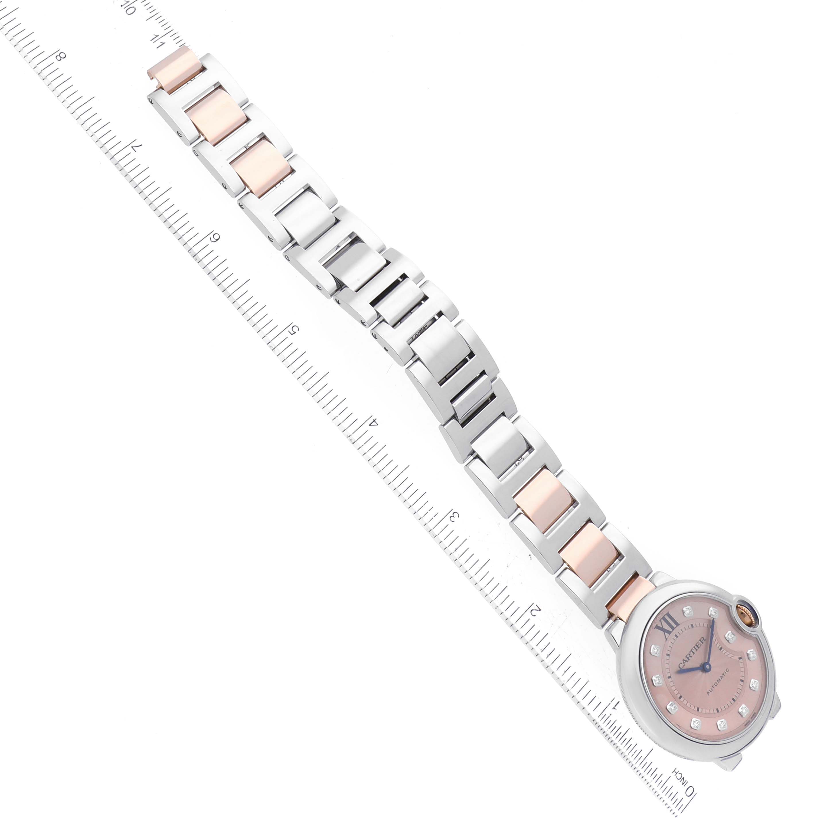 The image shows the Cartier Ballon Bleu WE902054 Women's Steel and Gold (two tone) Pink Dial WE902054 Women's Steel and Gold (two tone) Pink Dial watch laid flat with a focus on its band and face, alongside a ruler for scale.