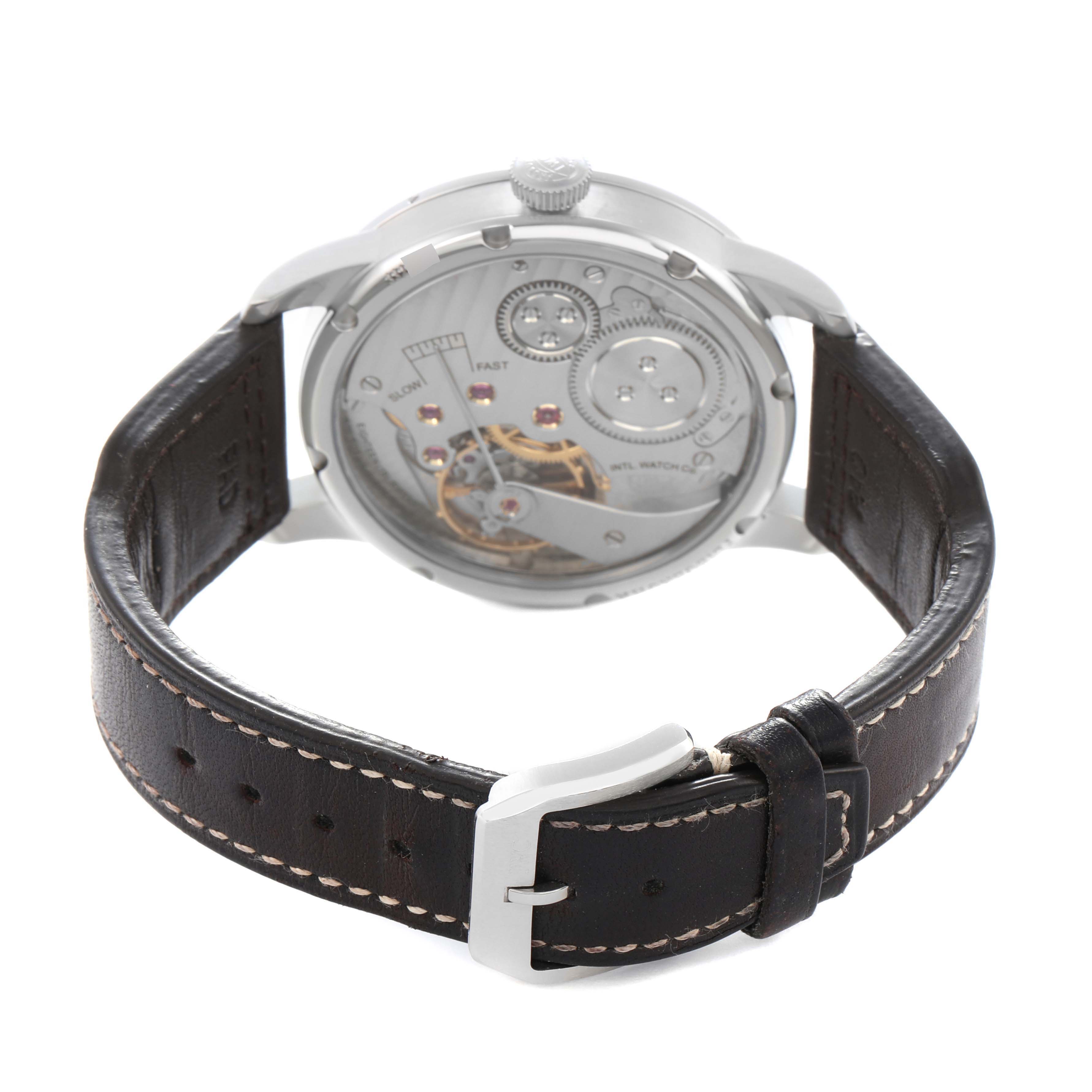 The IWC Pilot IW325401 Men
s Platinum Black Dial watch is shown from the rear, displaying its movement and a brown leather strap with a buckle.