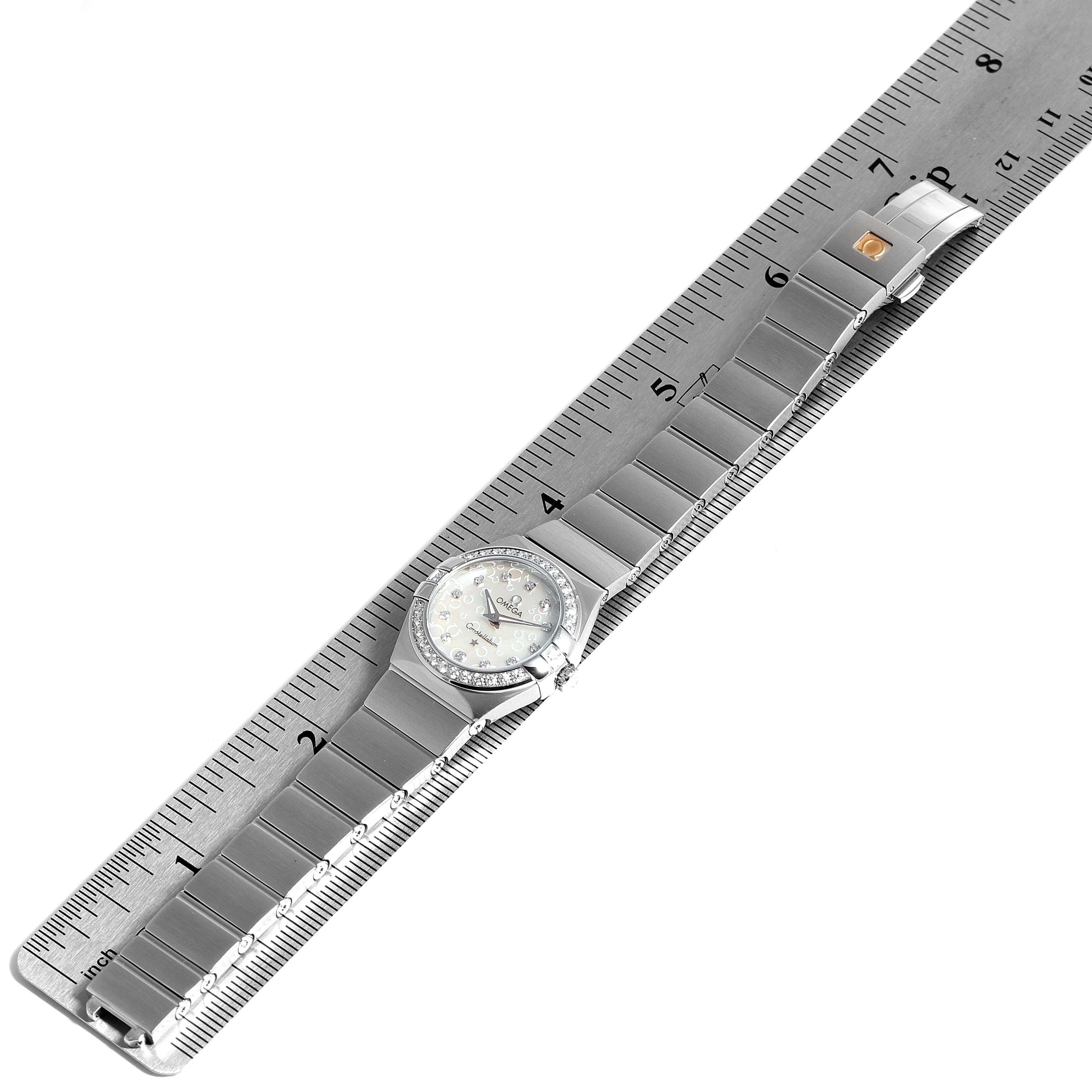 The image shows an Omega 123.15.24.60.52.001 Women's Stainless Steel Silver Dial 123.15.24.60.52.001 Women's Stainless Steel Silver Dial Constellation 27mm Diamond Ladies Watch 123.15.24.60.52.001 placed flat alongside a ruler, displaying its bracelet and face.