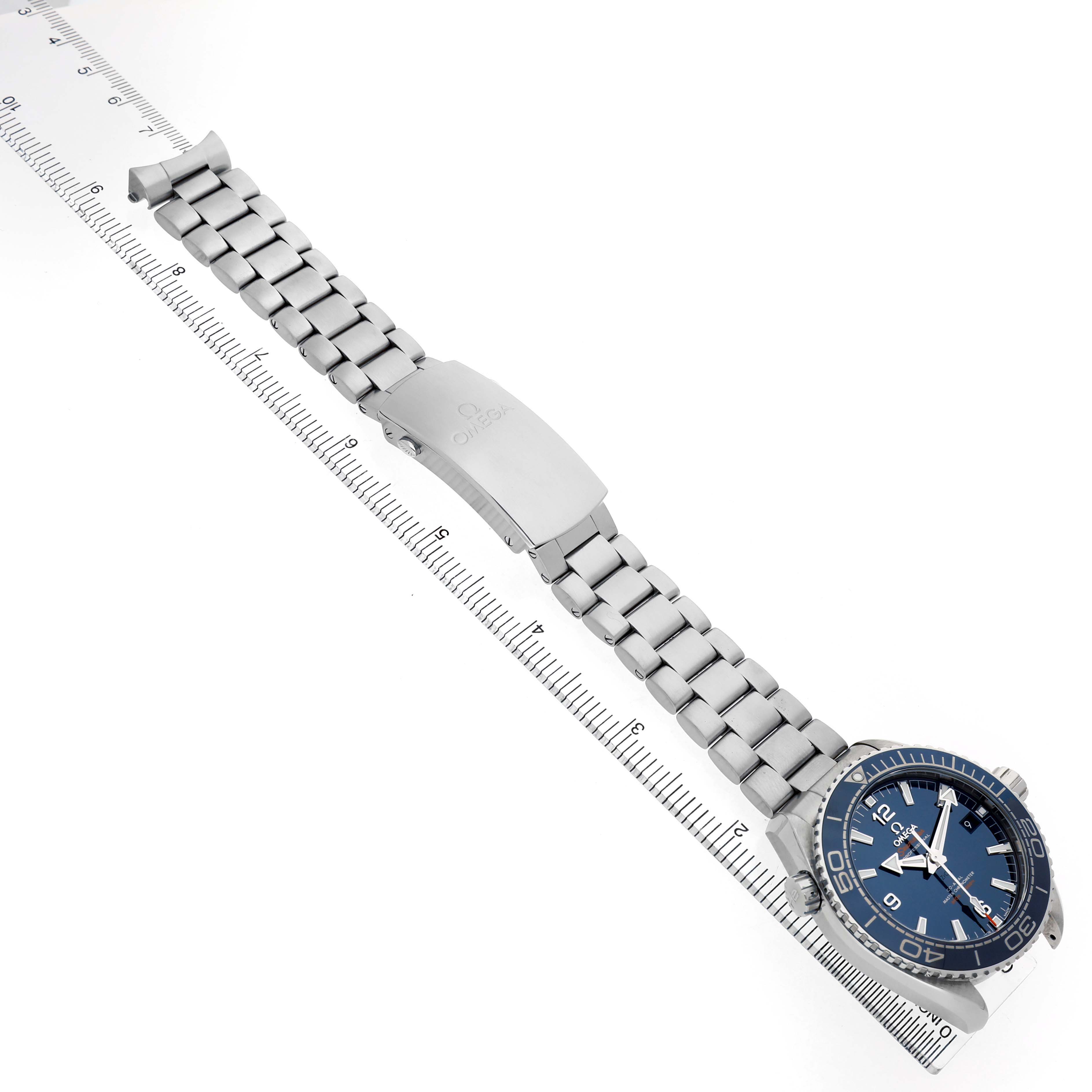 The Omega Planet Ocean 215.30.44.21.03.001 Men's Stainless Steel Blue Dial watch is shown at an angle, highlighting its bracelet, clasp, and blue face next to a ruler.