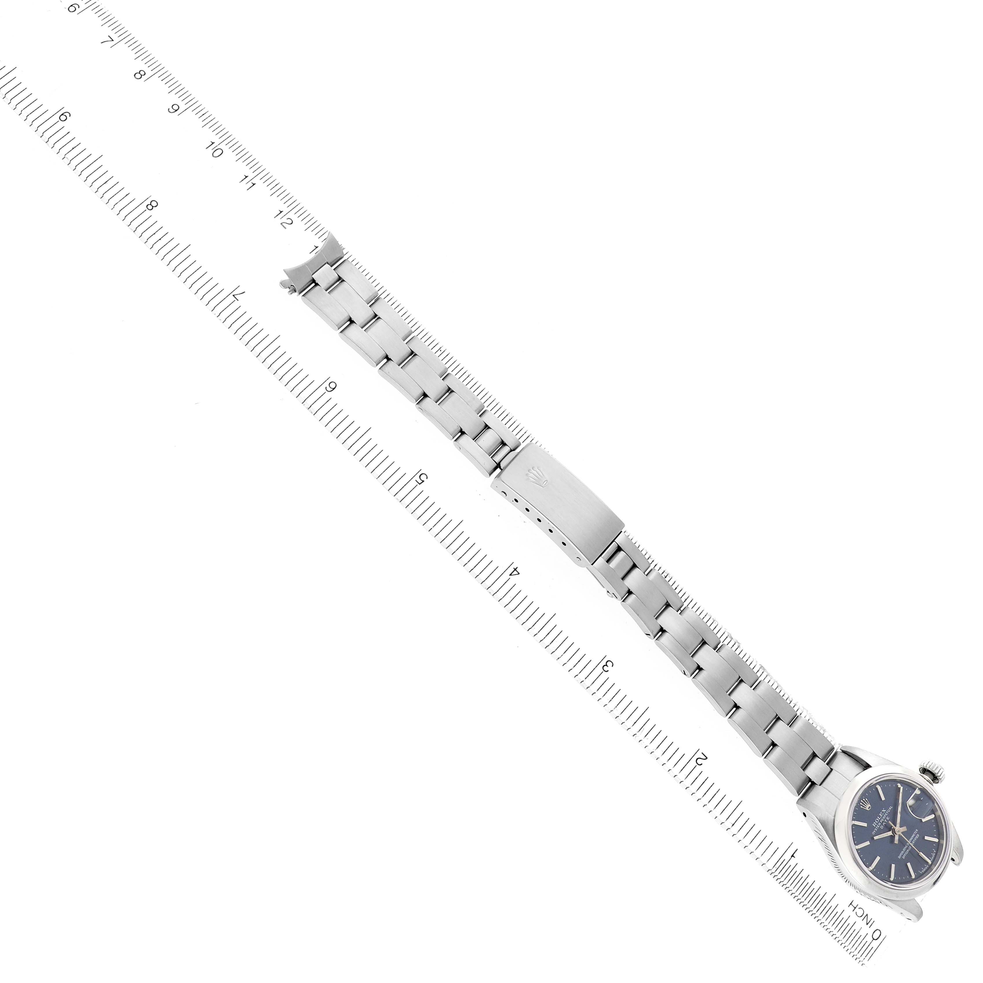 The Rolex Date 69160 Women
s Stainless Steel Blue Dial model watch is shown from a top view, displaying the watch face, bracelet, and clasp alongside a ruler for scale.