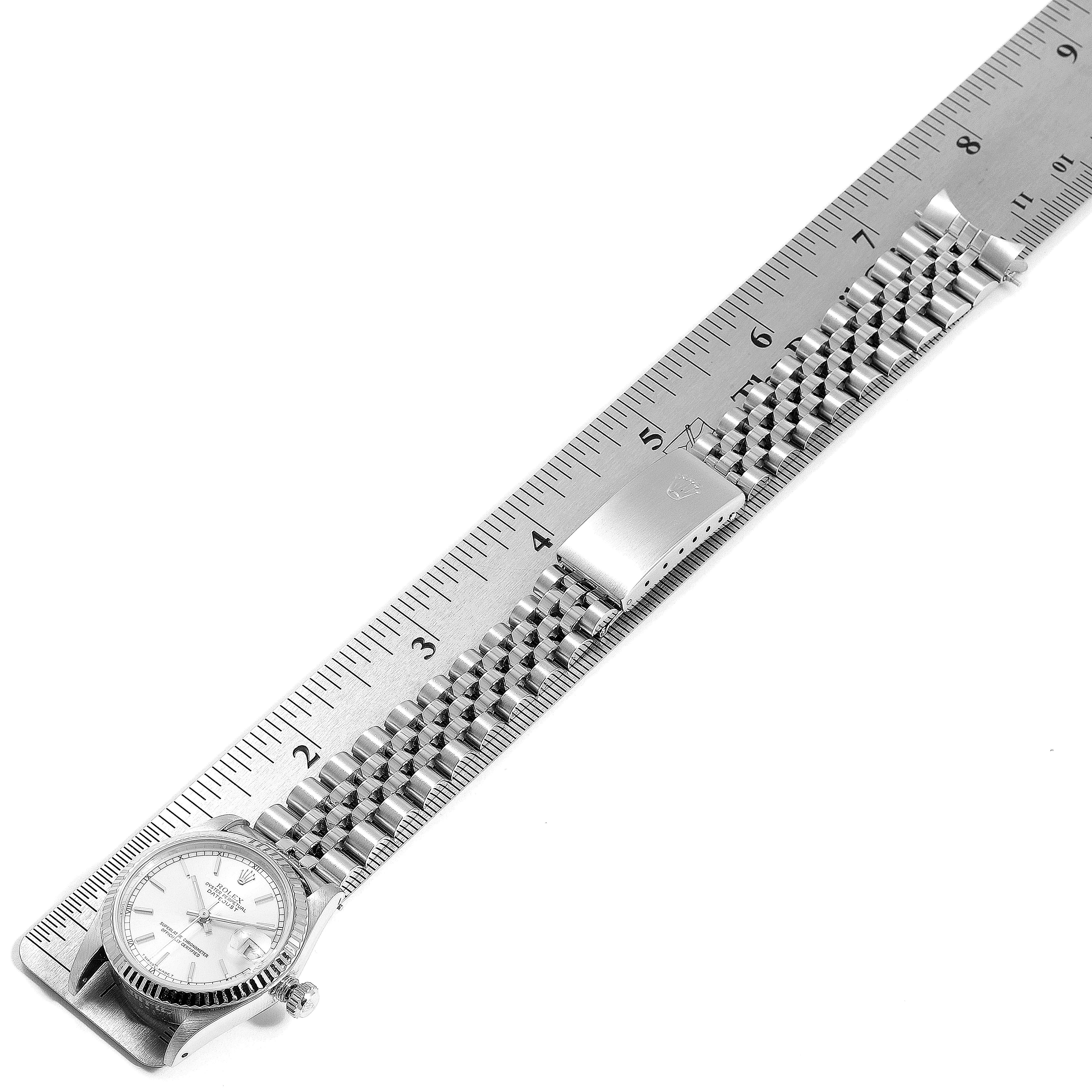 The image shows a Rolex Mid-Size 68274 Women
s Stainless Steel Silver Dial 68274 Women
s Stainless Steel Silver Dial watch laid flat next to a ruler, displaying the face, bracelet, and clasp from an overhead view.