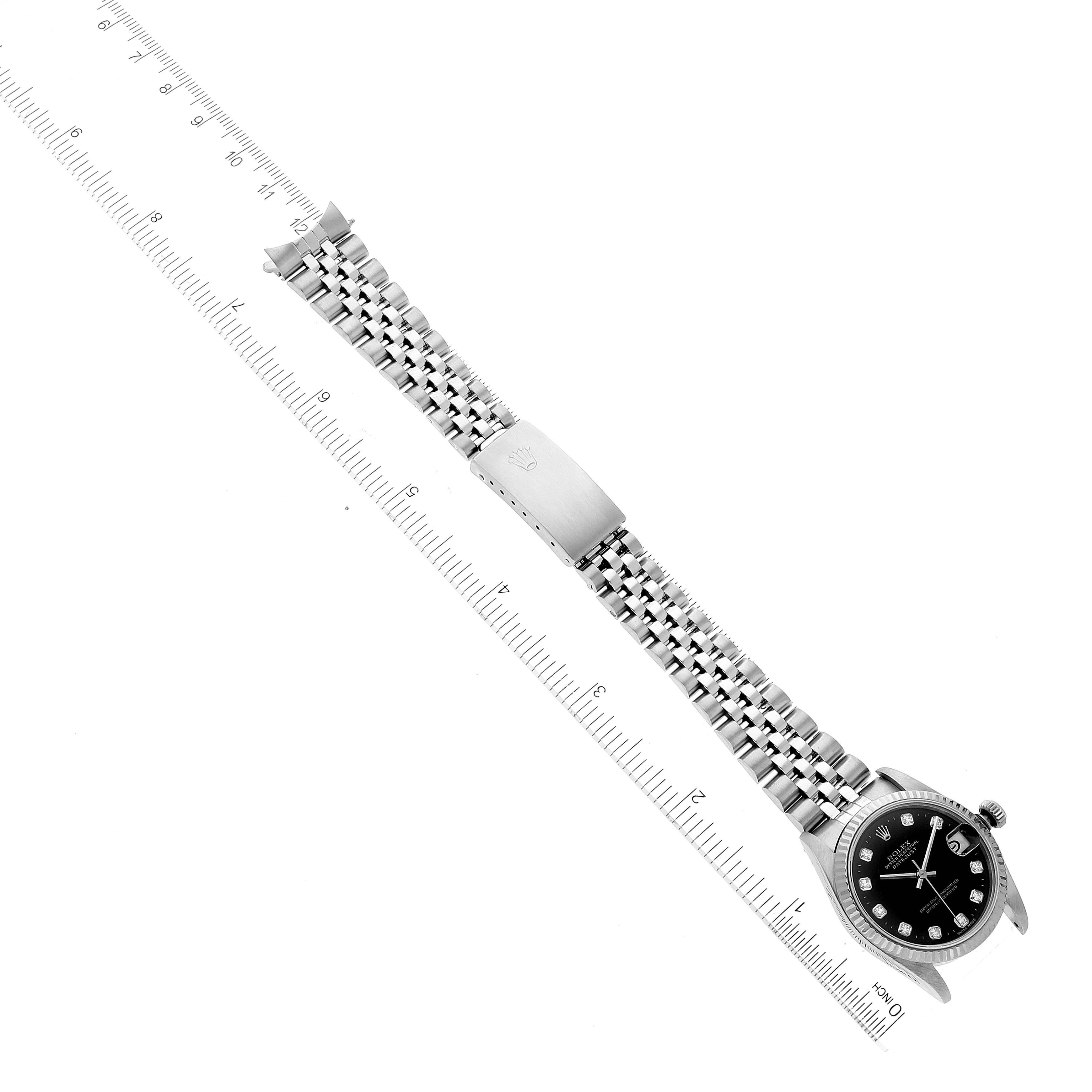 The watch is a Mid-Size Rolex model shown from a top-down angle, displaying the face, bezel, band, clasp, and is laid beside a ruler for scale.