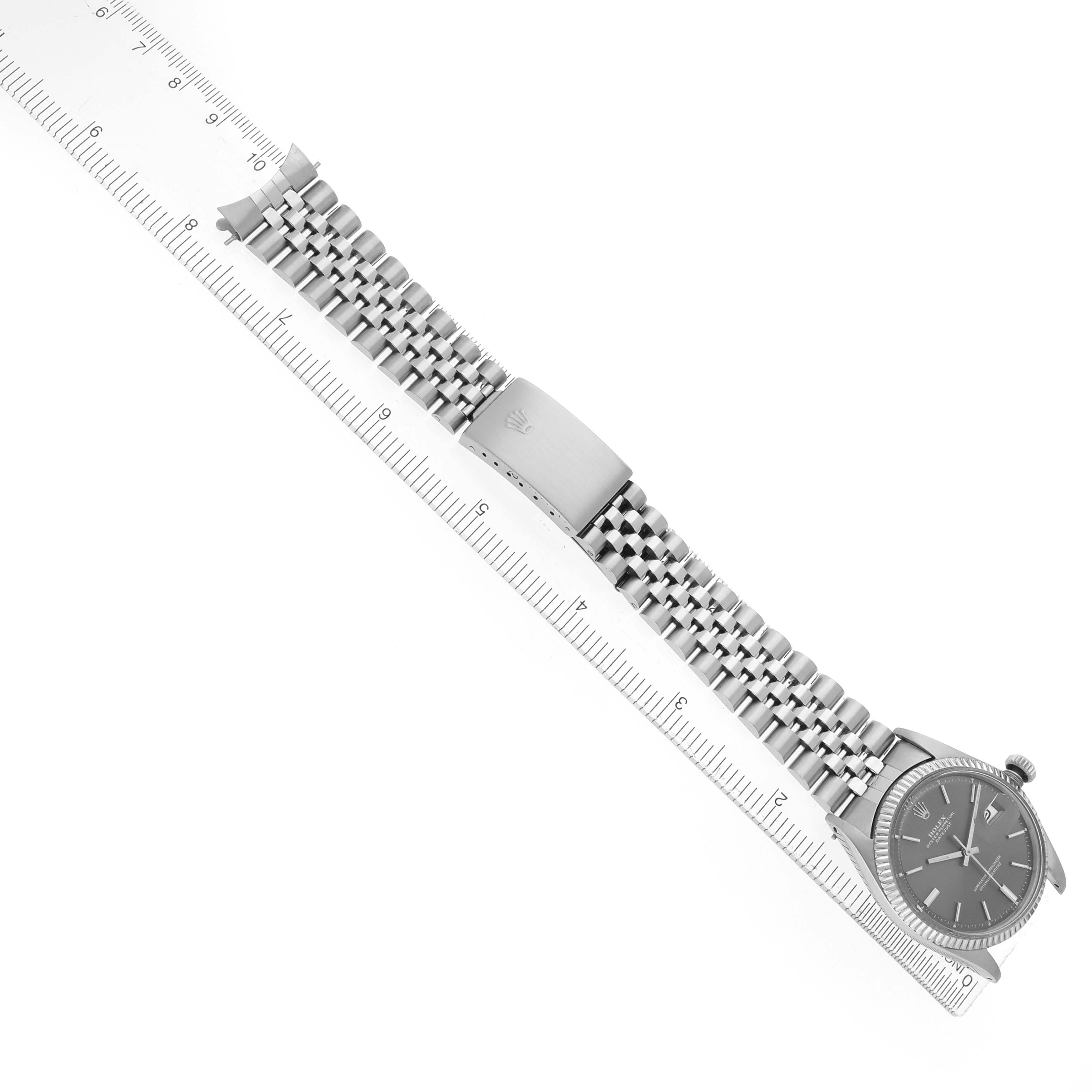 The Rolex Datejust 1601 Men
s Stainless Steel Grey Dial watch is shown from a top-down angle, displaying the face, bracelet, and clasp aligned with a ruler.