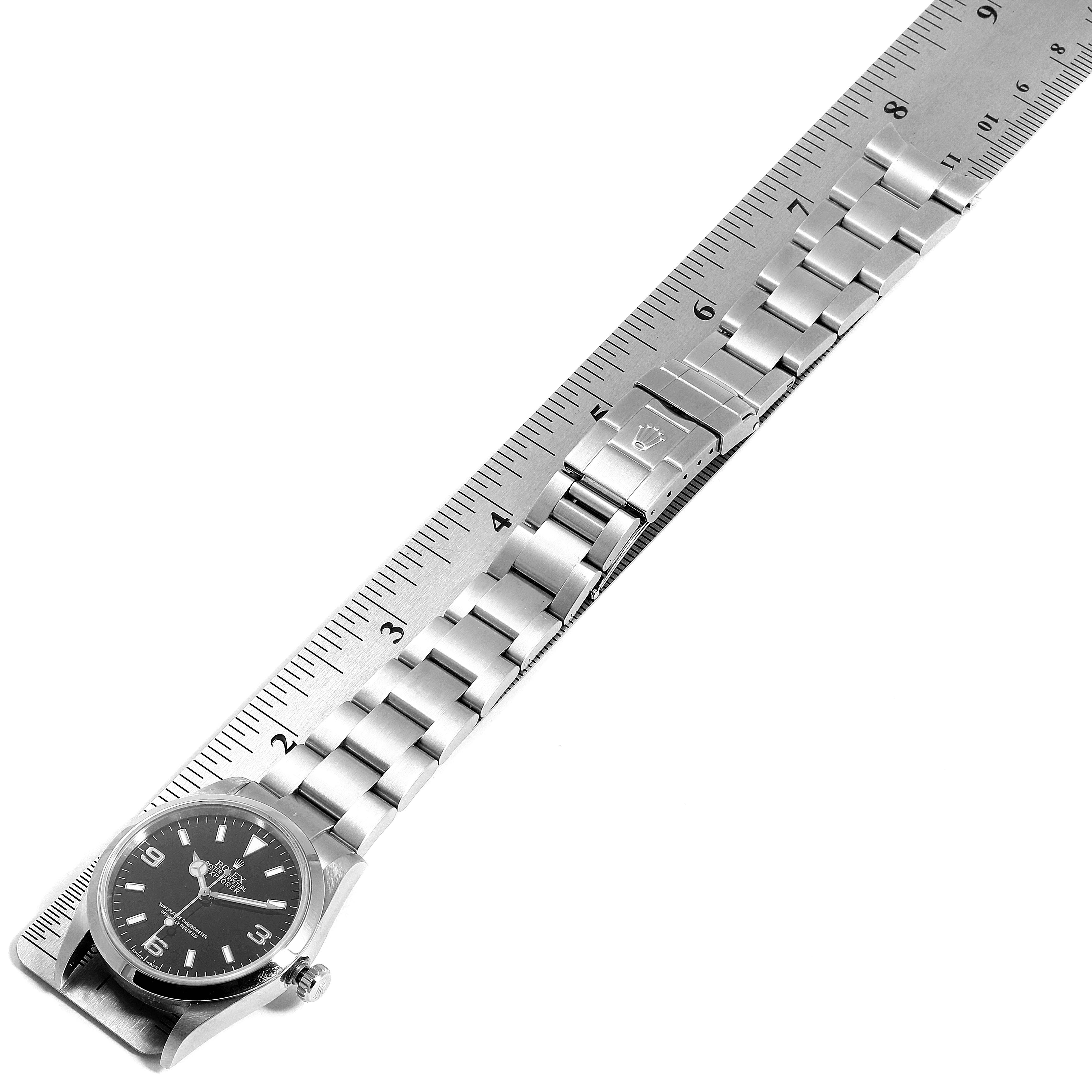 The image shows a top-down view of a Rolex Explorer 114270 Men
s Stainless Steel Black Dial 114270 Men
s Stainless Steel Black Dial watch, displaying the face and entire metal bracelet alongside a ruler.