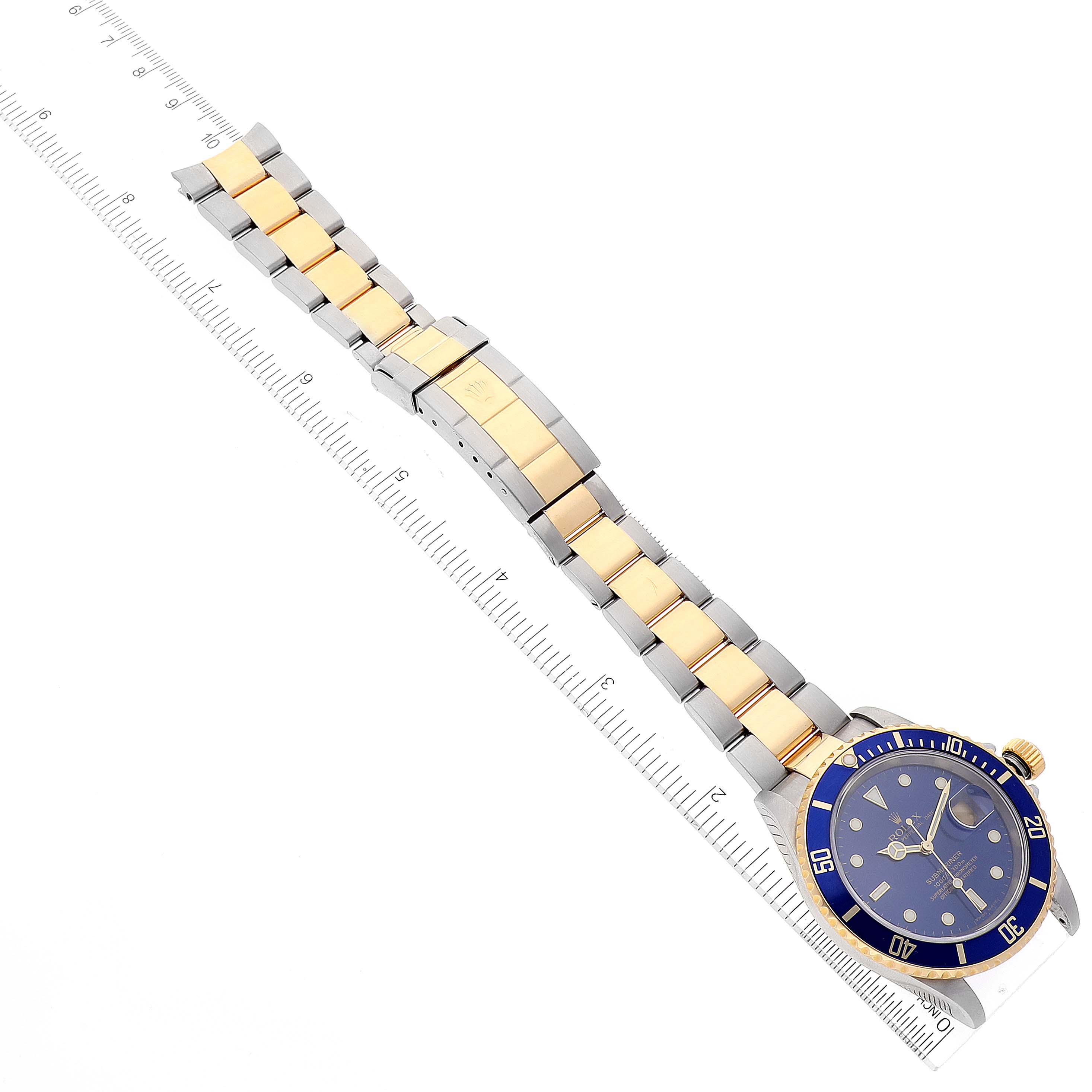 The image shows a Rolex Submariner 16613 Men
s Steel and Gold (two tone) Blue Dial 16613 Men
s Steel and Gold (two tone) Blue Dial watch with a blue and gold bezel, and a two-tone metal bracelet alongside a ruler for scale.