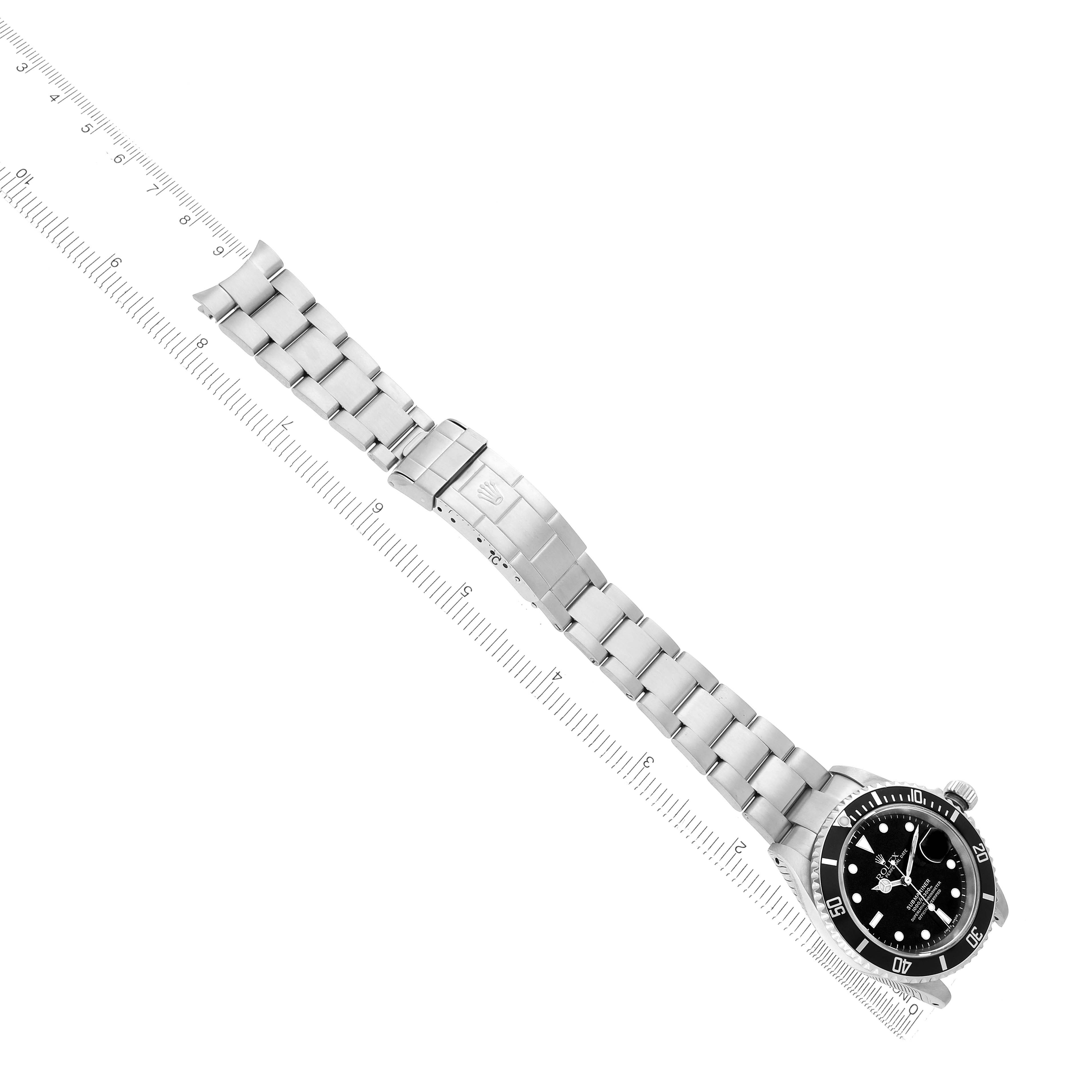 The Rolex Submariner 16610 Men
s Stainless Steel Black Dial watch is shown at an angled view, displaying its bracelet, clasp, and face alongside a ruler for size reference.