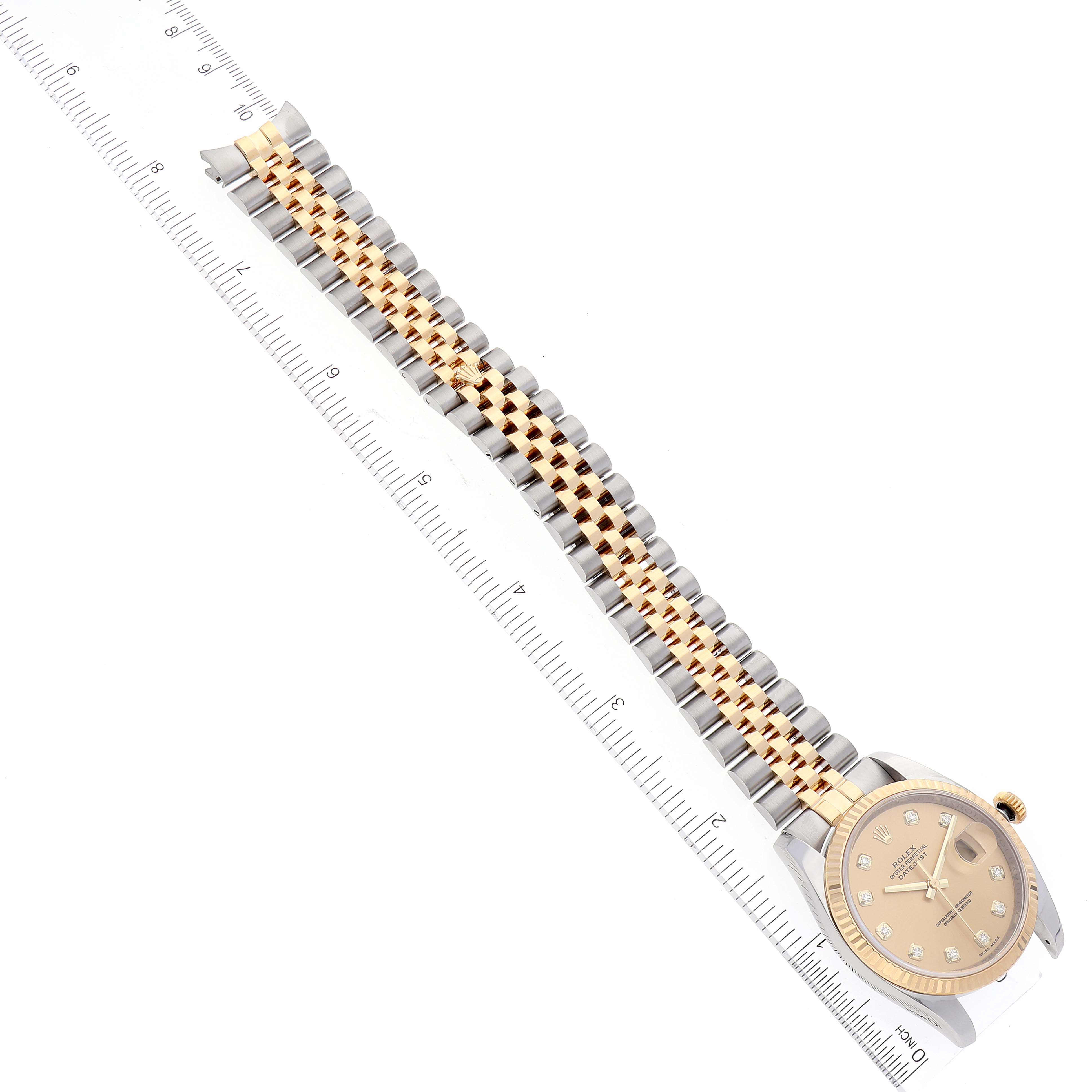 The Rolex Datejust 116233 Men's Steel and Gold (two tone) Champagne Dial 116233 Men's Steel and Gold (two tone) Champagne Dial watch is shown from an overhead angle, displaying its band and watch face alongside a ruler.