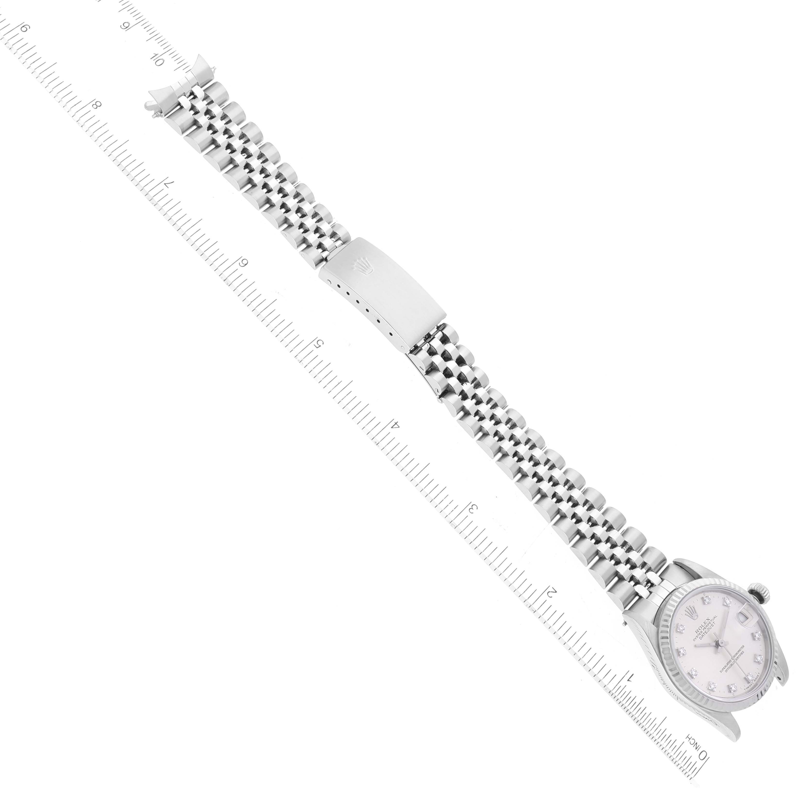 The Mid-Size Rolex watch is shown from an overhead angle, displaying its face, bracelet, and clasp next to a marked ruler.