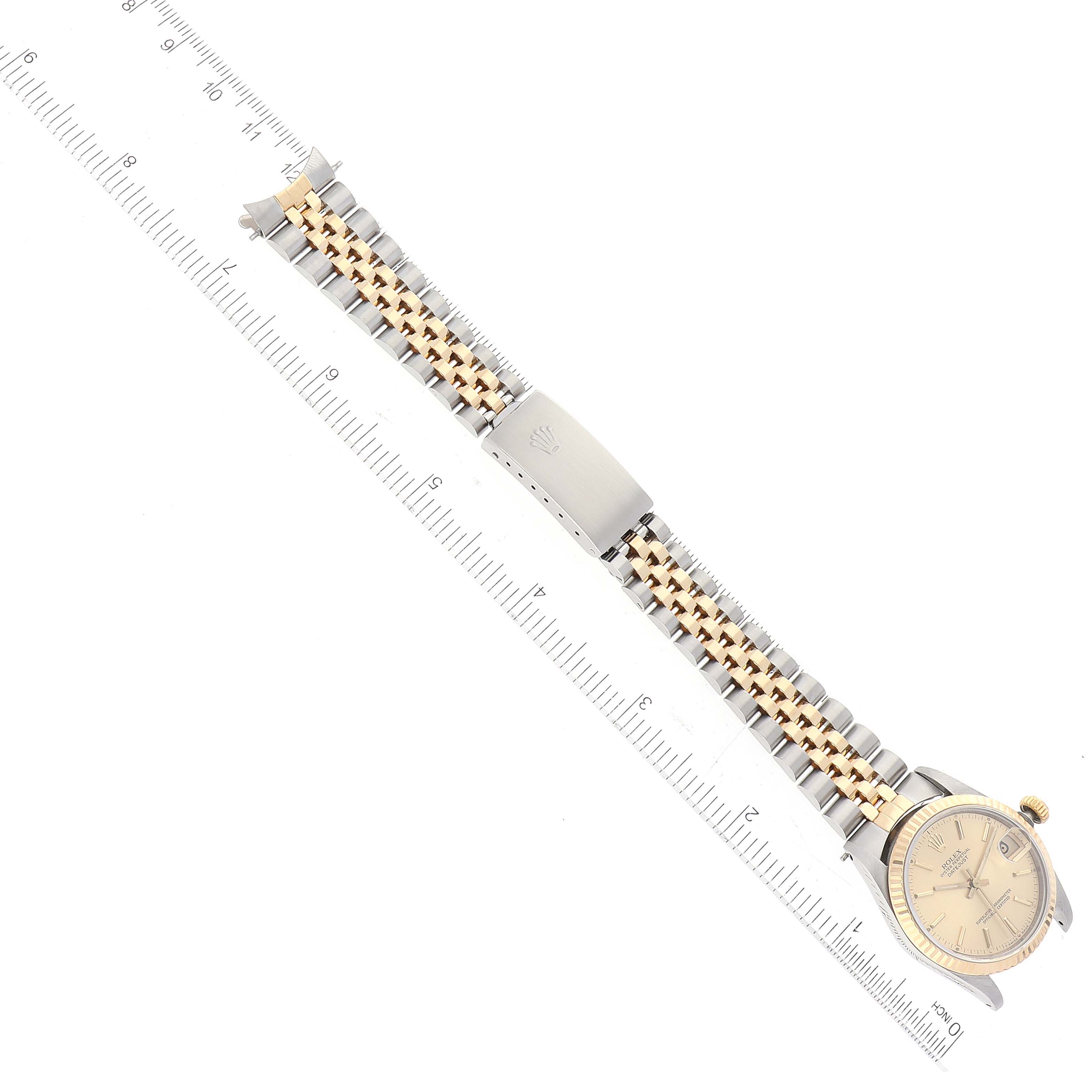The Rolex Mid-Size 68273 Women's Stainless Steel Champagne Dial 68273 Women's Stainless Steel Champagne Dial watch is shown from a top-down angle, highlighting its face, bracelet, and clasp alongside a ruler.