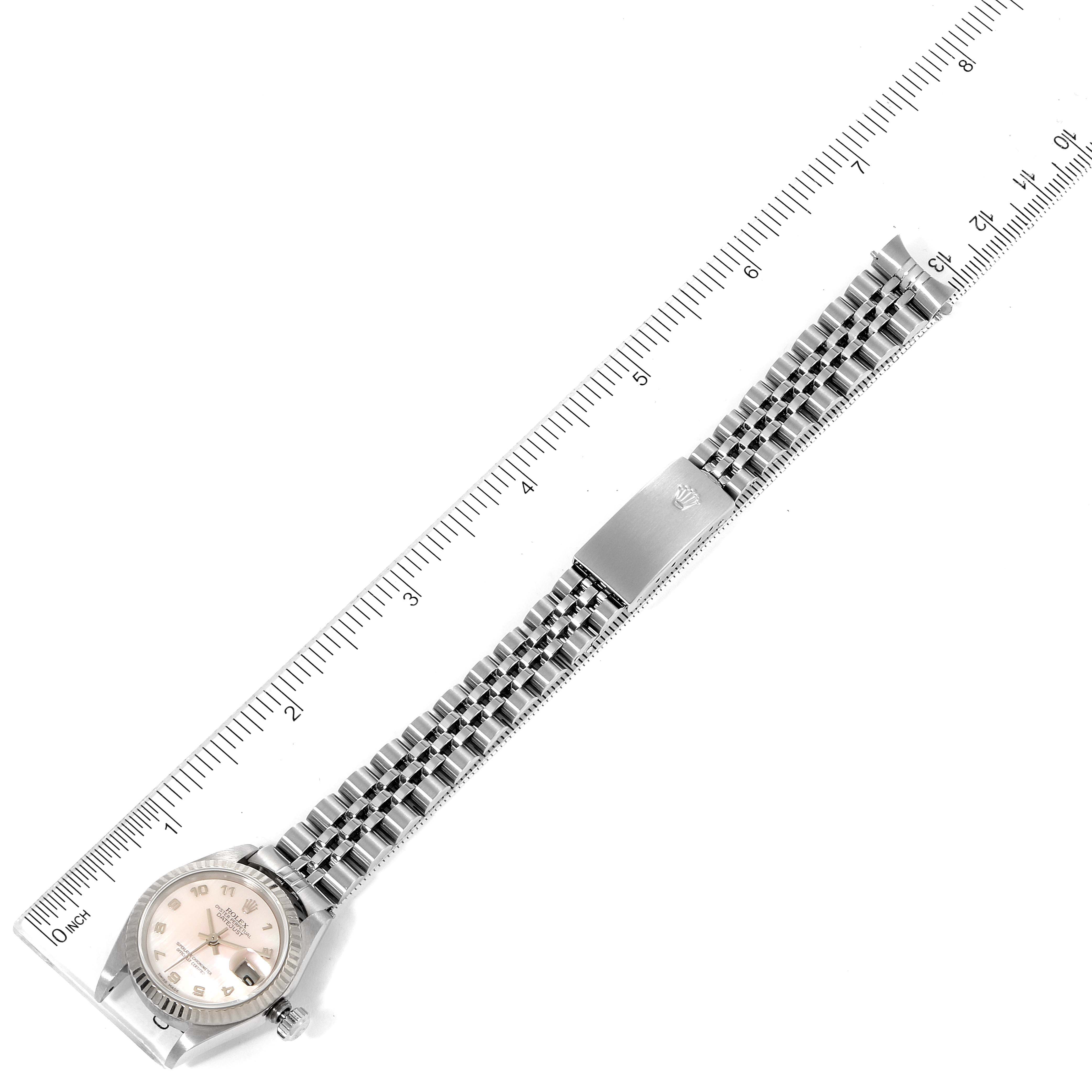 The image shows a top view of a Rolex Datejust 79174 Women
s Stainless Steel Mother of Pearl Dial 79174 Women
s Stainless Steel Mother of Pearl Dial watch, including the face, bezel, and full metal bracelet positioned against a ruler.