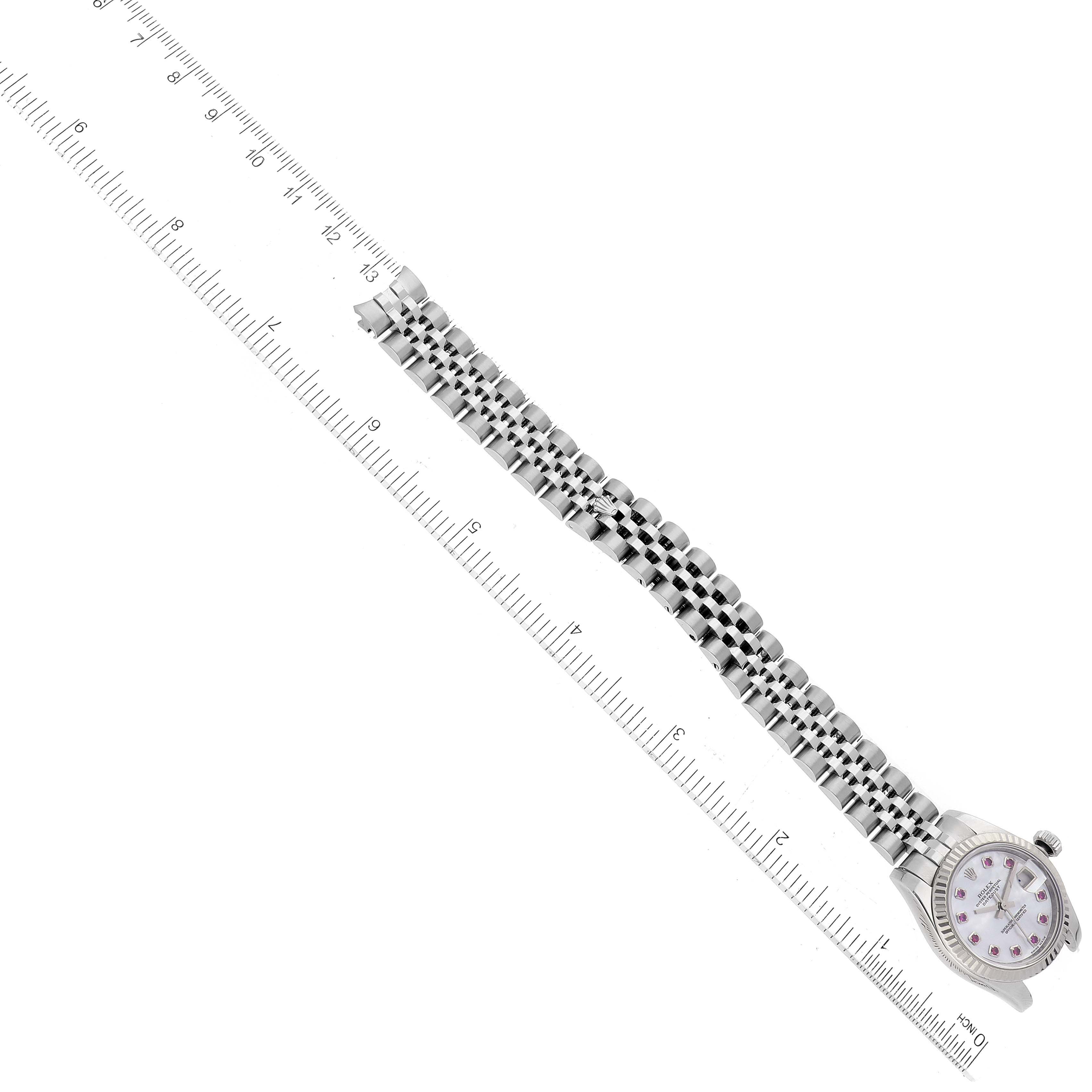 This image shows a Rolex Datejust 179174 Women
s Stainless Steel Mother of Pearl Dial 179174 Women
s Stainless Steel Mother of Pearl Dial watch laying flat, with its face at the bottom left and the metal bracelet aligned along a ruler.