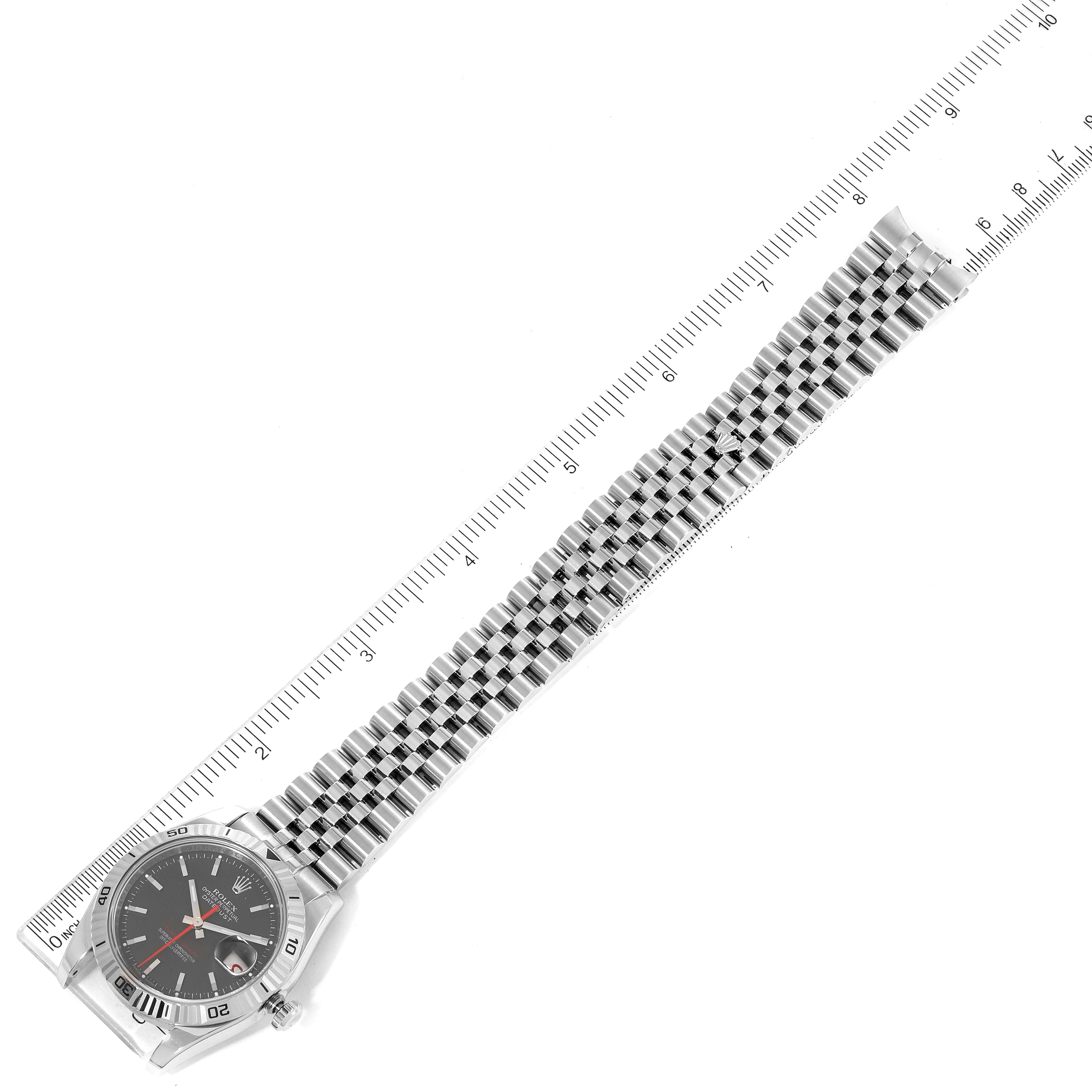 This image shows a top-down view of the Rolex Turn-o-Graph 116264 Men
s Stainless Steel Black Dial 116264 Men
s Stainless Steel Black Dial watch, displaying its face, bezel, and metal bracelet beside a measuring ruler.