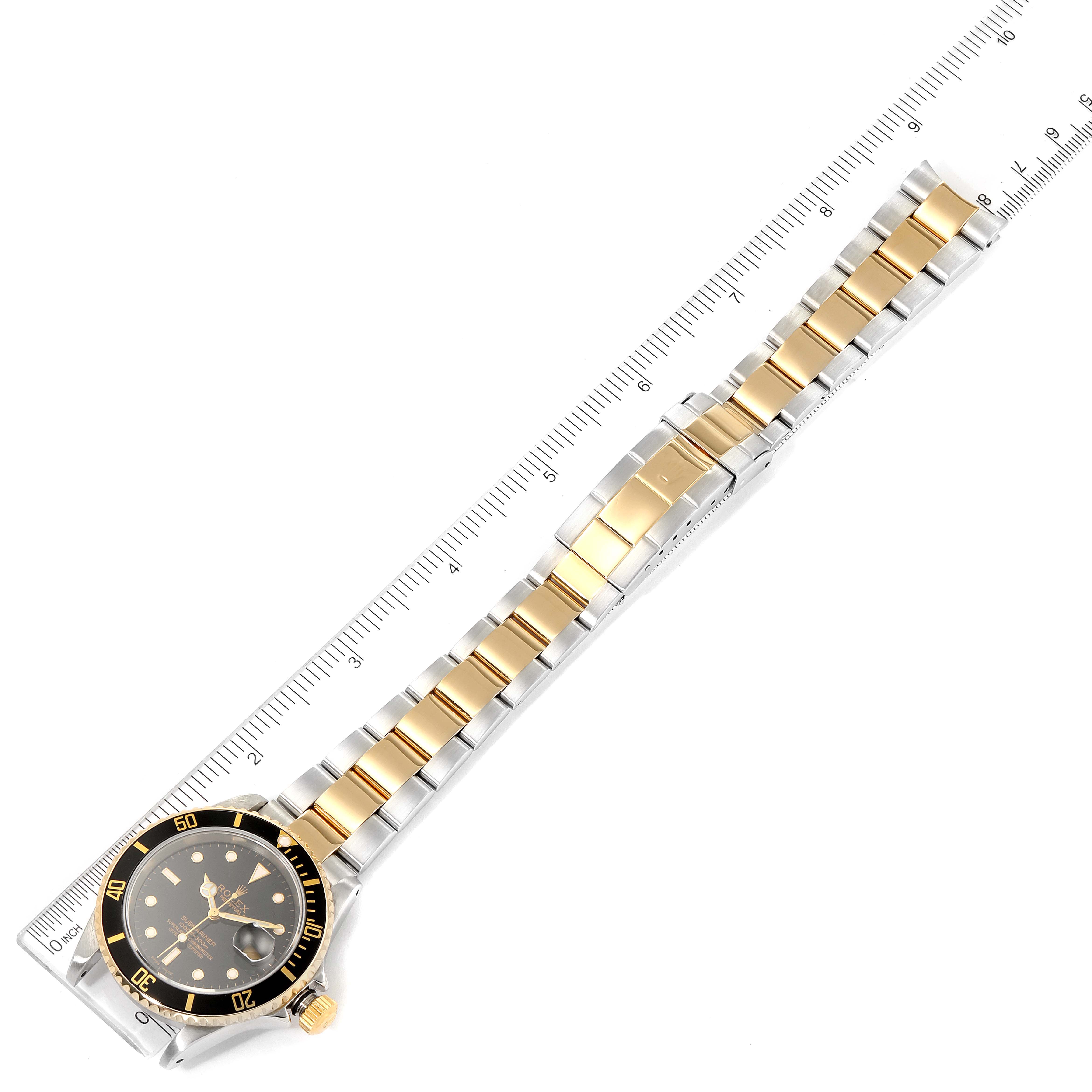 The image displays an overhead view of a Rolex Submariner 16613 Men's Steel and Gold (two tone) Black Dial 16613 Men's Steel and Gold (two tone) Black Dial watch, including the face, bezel, and bracelet, aligned with a ruler.