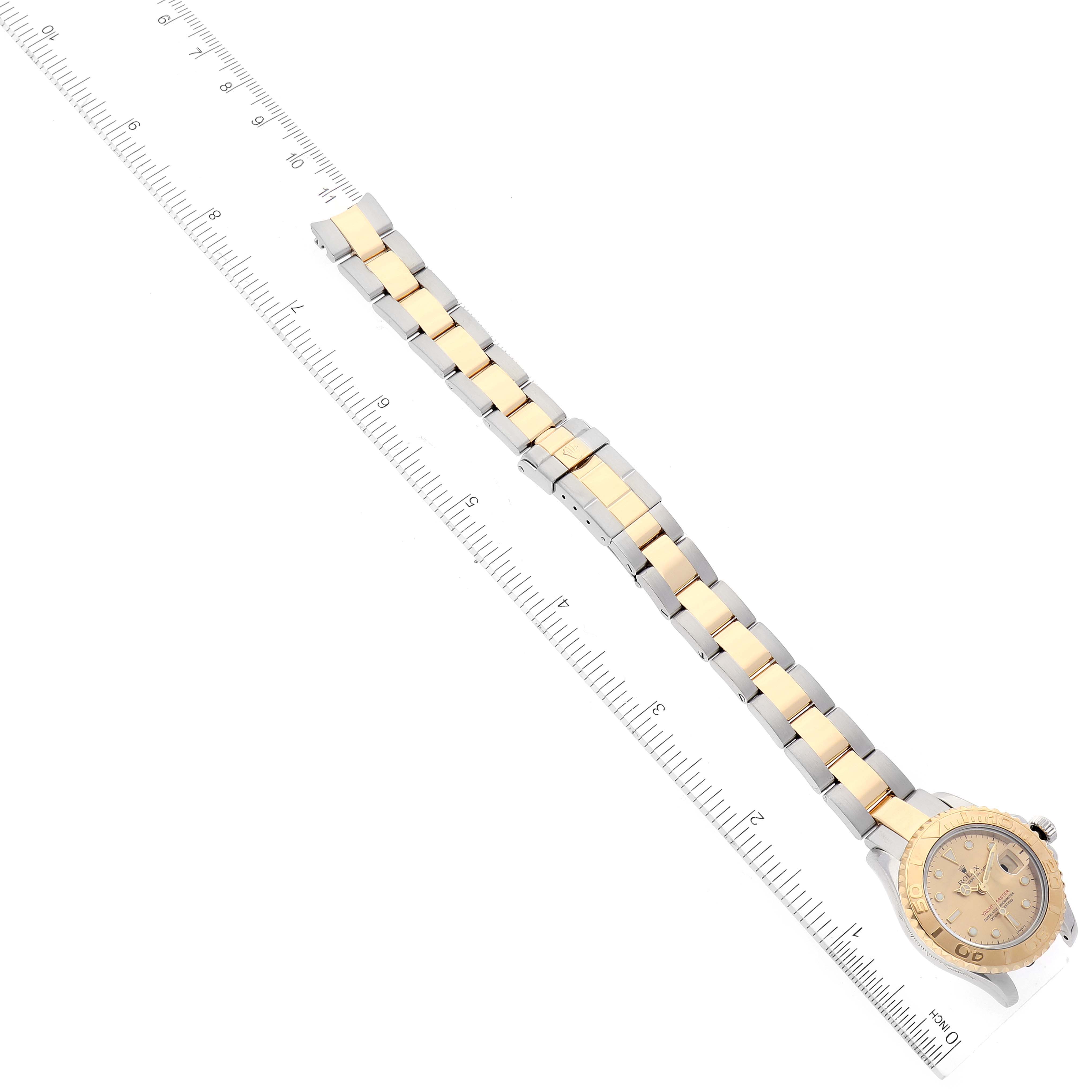 The image shows a top-down view of a Rolex Yacht-Master 69623 Women's Steel and Gold (two tone) Champagne Dial 69623 Women's Steel and Gold (two tone) Champagne Dial watch, highlighting its bracelet and dial beside a ruler for scale.