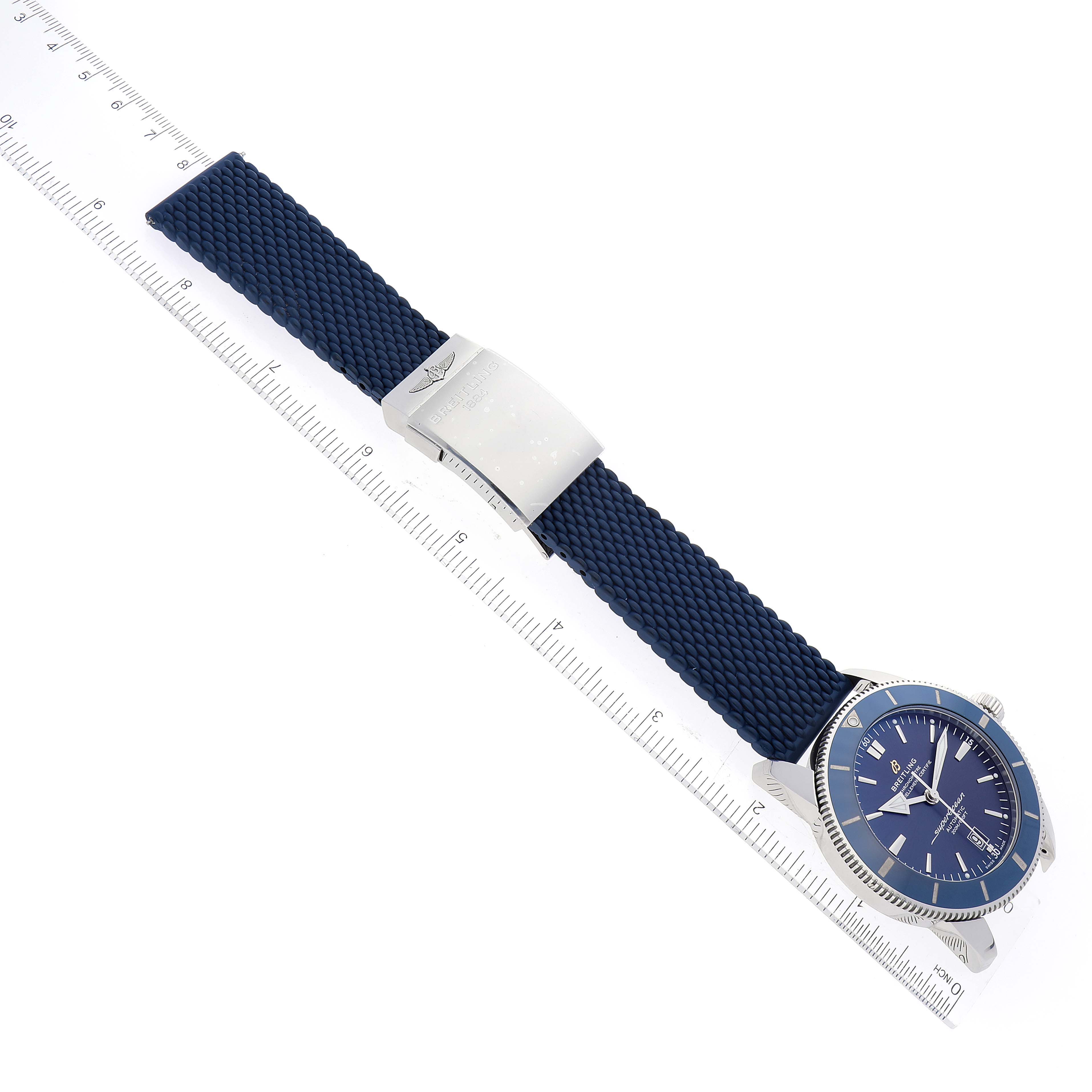 The image shows a top-view angle of the Breitling Superocean AB2020 Men's Stainless Steel Blue Dial AB2020 Men's Stainless Steel Blue Dial watch, highlighting its blue strap and dial along with a clasp and a ruler for scale.