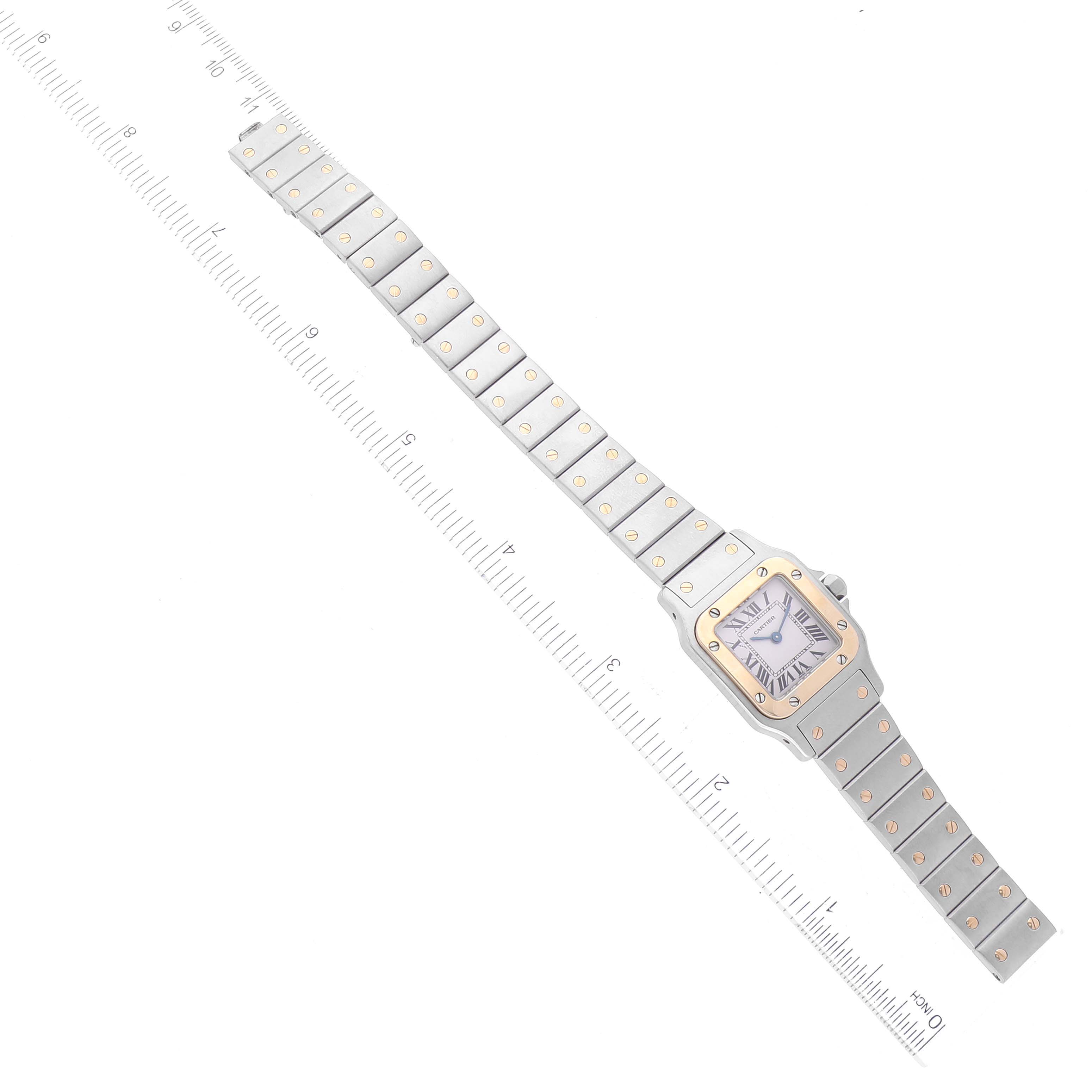 The image shows a top-down view of a Cartier Santos W20012C4 Women's Steel and Gold (two tone) Silver Dial W20012C4 Women's Steel and Gold (two tone) Silver Dial watch, including the face and full bracelet, with a ruler for size reference.