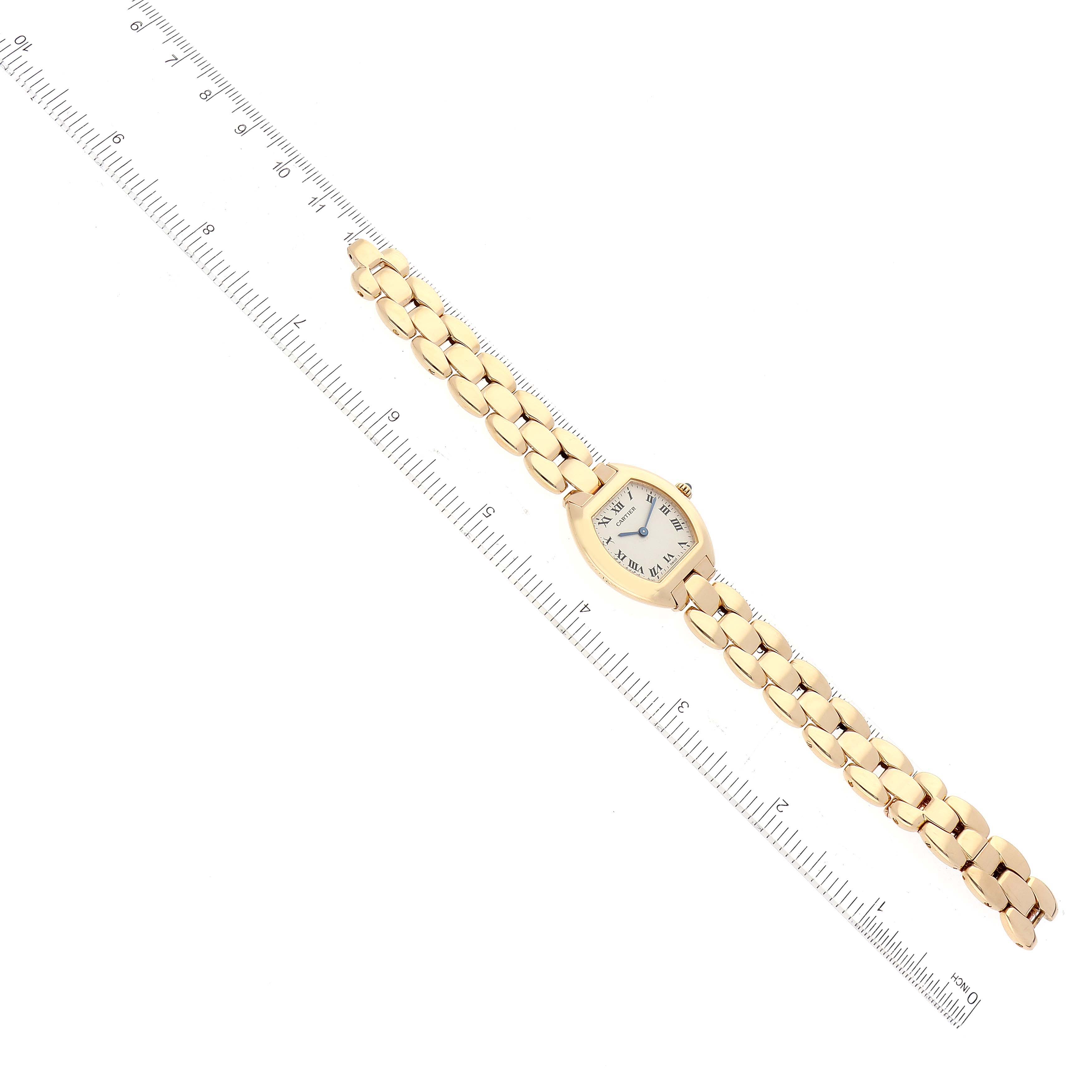 The image shows a top view of a Cartier Tortue 1945 Women's Yellow Gold Silver Dial 1945 Women's Yellow Gold Silver Dial watch, including the entire watch and its gold bracelet laid next to a ruler.