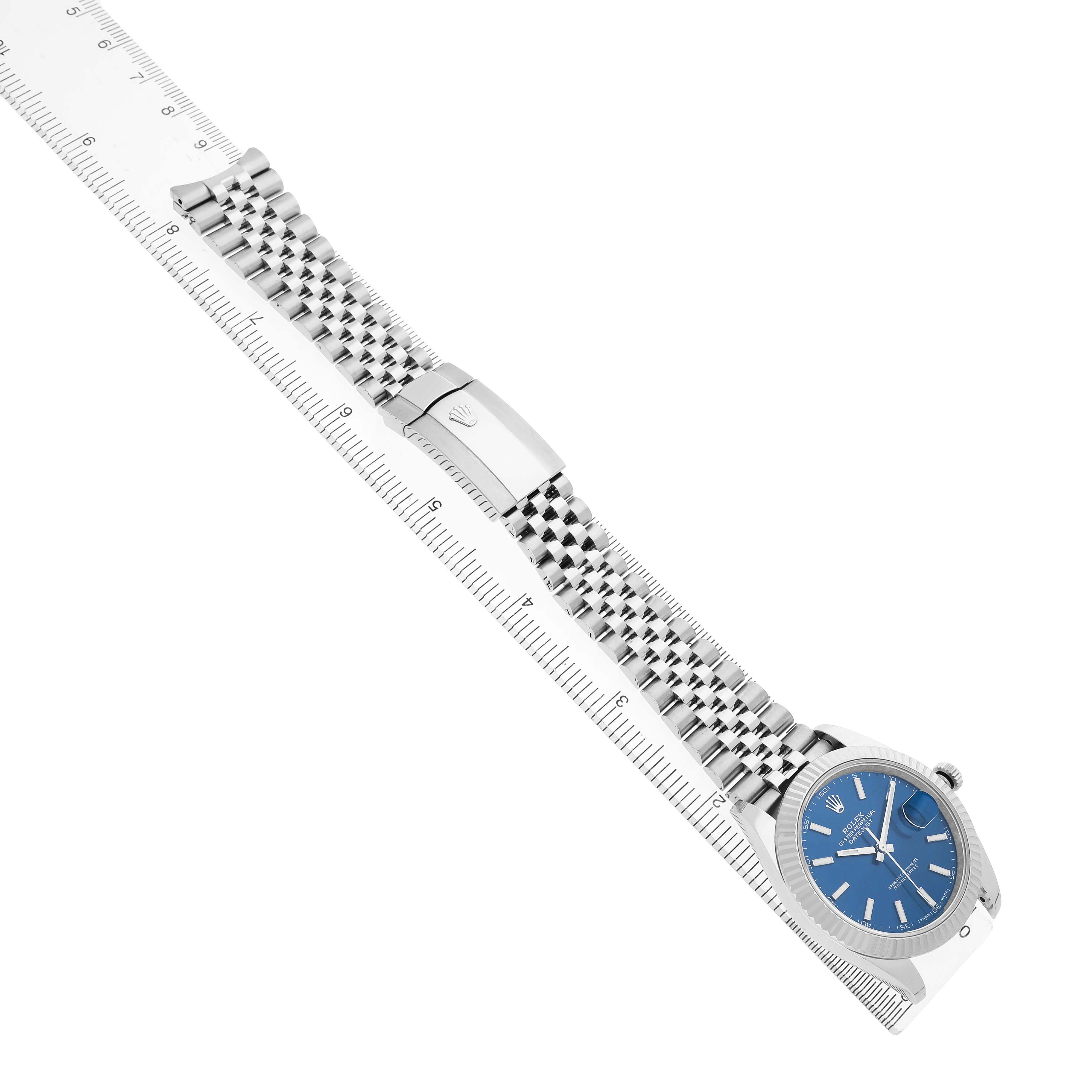 The Rolex Datejust 41 126334 Men's White Gold Black Dial is shown at an oblique angle, featuring the watch face, bracelet, and clasp on a ruler.