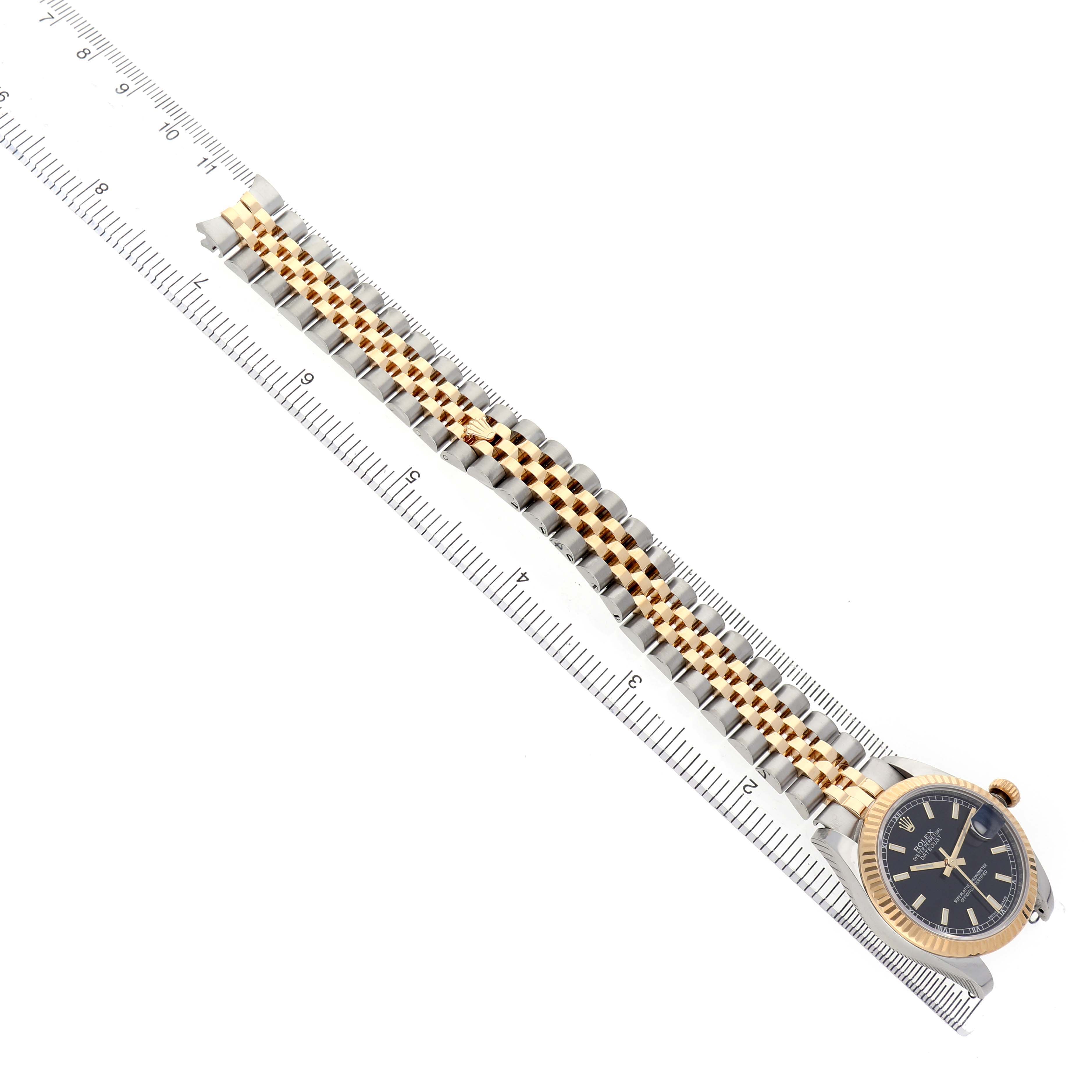 The Rolex Mid-Size 178273 Women's Steel and Gold (two tone) Black Dial watch is shown from an overhead angle, displaying the bracelet, bezel, and dial, alongside a ruler for scale.