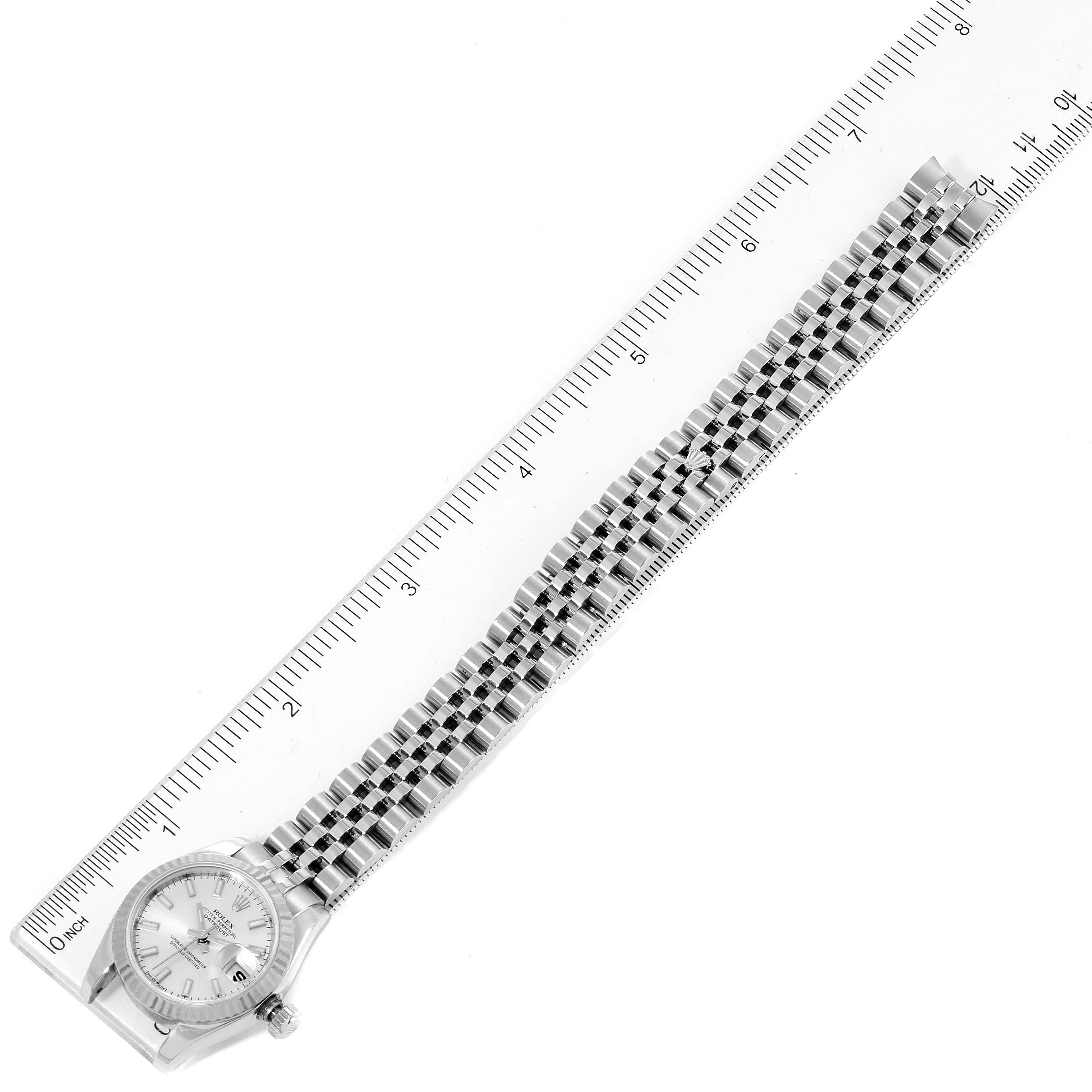 The image shows a Rolex Datejust 179174 Women
s Stainless Steel Silver Dial 179174 Women
s Stainless Steel Silver Dial watch laid flat next to a ruler, highlighting the bracelet and face.