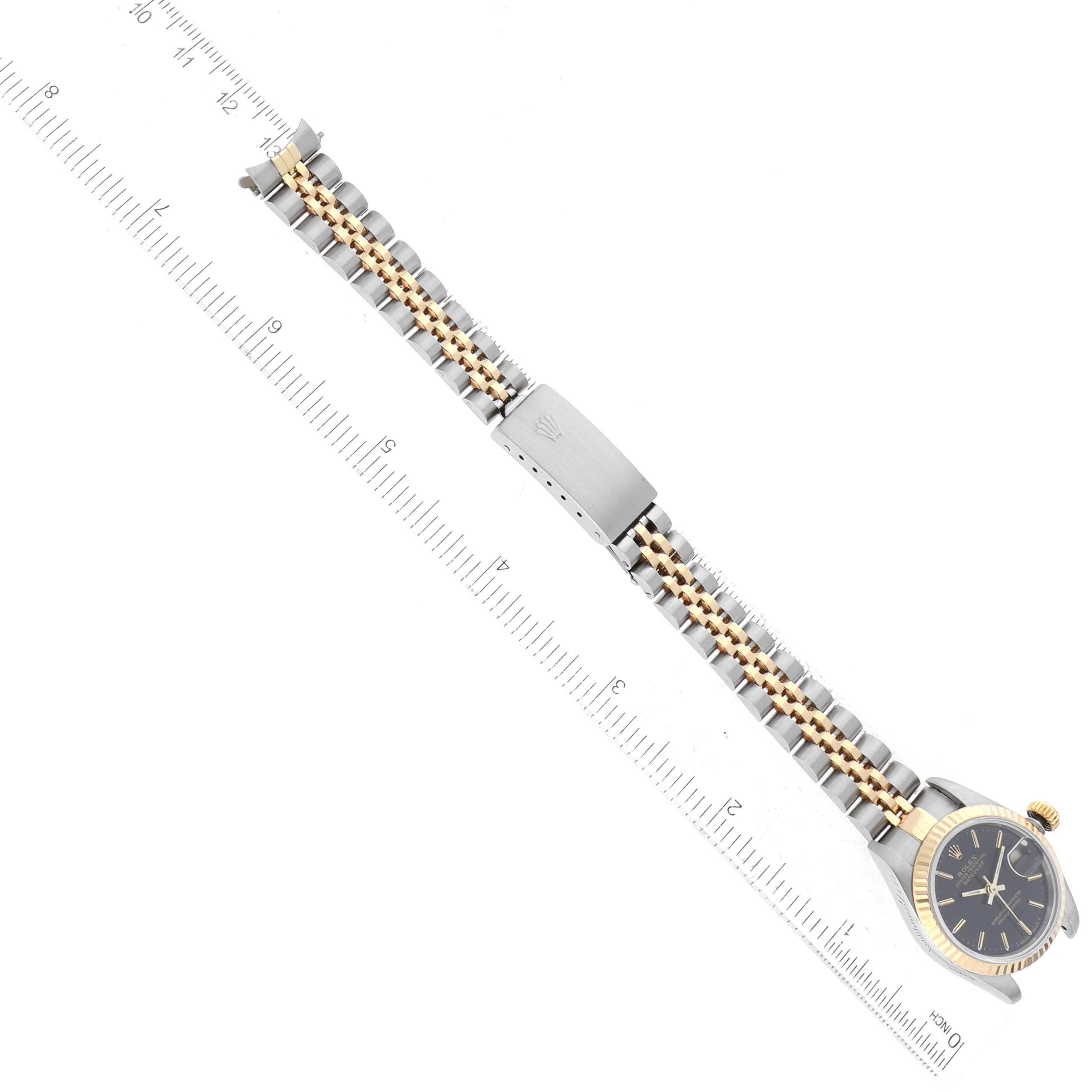 The image displays a top view of a Rolex Datejust 69173 Women's Steel and Gold (two tone) Black Dial 69173 Women's Steel and Gold (two tone) Black Dial watch showing the face, bracelet, and clasp alongside a ruler for scale.