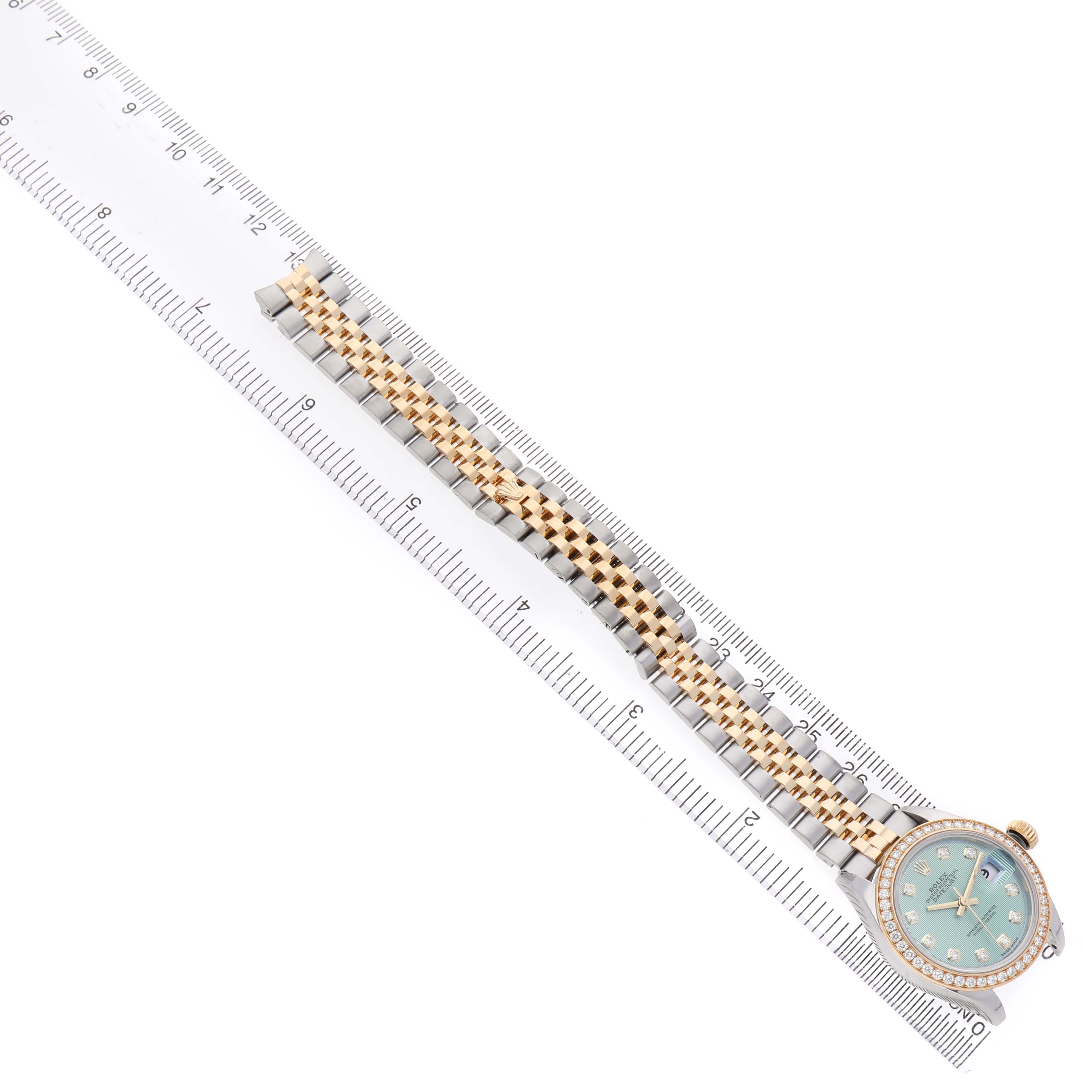 The Rolex Datejust 279383 Women's Steel and Gold (two tone) Green Dial watch is shown from a top-down angle, displaying the dial and full bracelet next to a ruler.