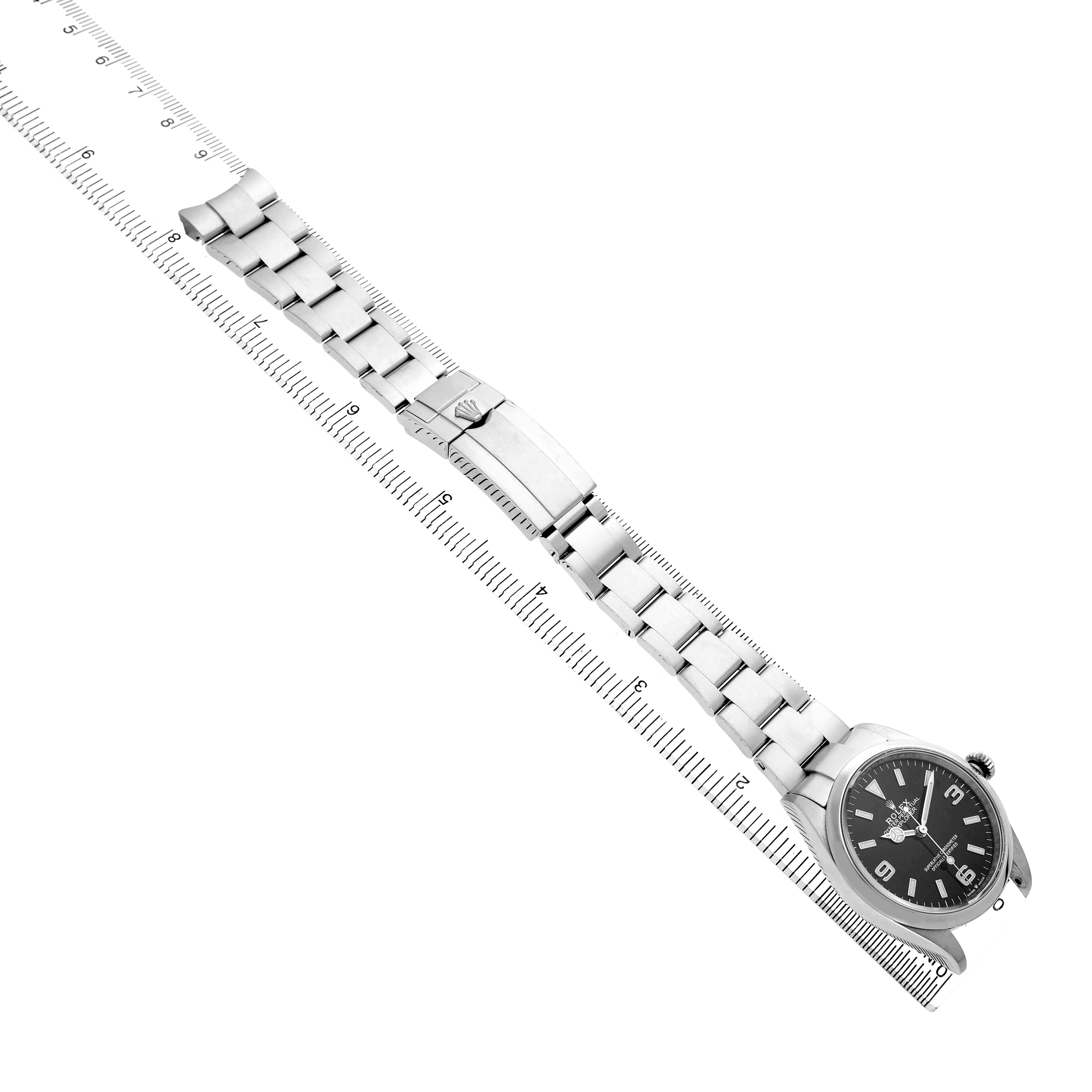 The Rolex Explorer 124270 Men's Stainless Steel Black Dial watch is shown from an overhead angle, displaying the face, bracelet, and clasp alongside a ruler for scale.