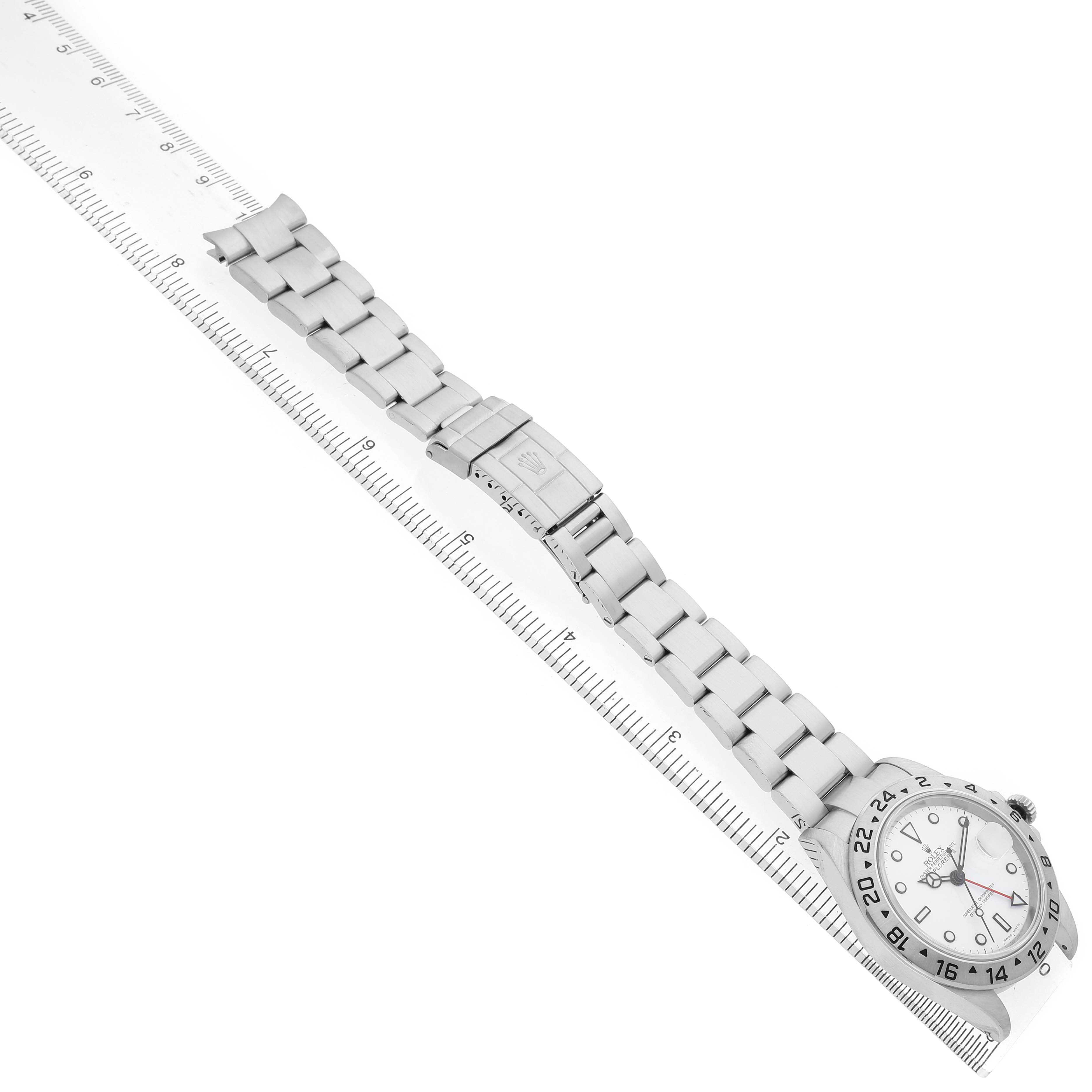The Rolex Explorer 16570 Men's Stainless Steel White Dial watch is shown from an overhead angle, displaying the full face, bracelet, and clasp alongside a ruler.