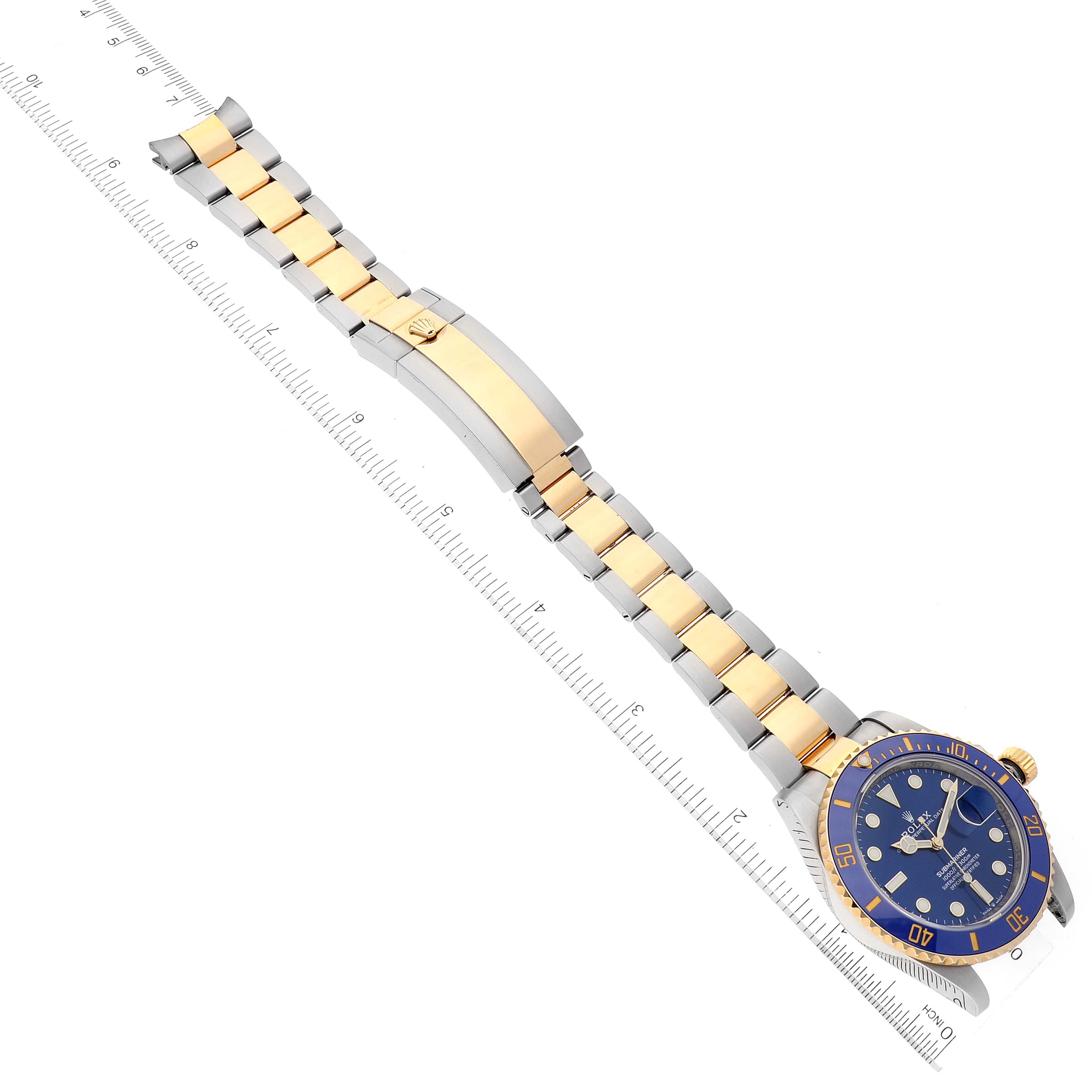 The image shows a Rolex Submariner 126613 Men's Steel and Gold (two tone) Blue Dial 126613 Men's Steel and Gold (two tone) Blue Dial watch laid flat with its face, bracelet, and clasp visible, alongside a ruler for scale.
