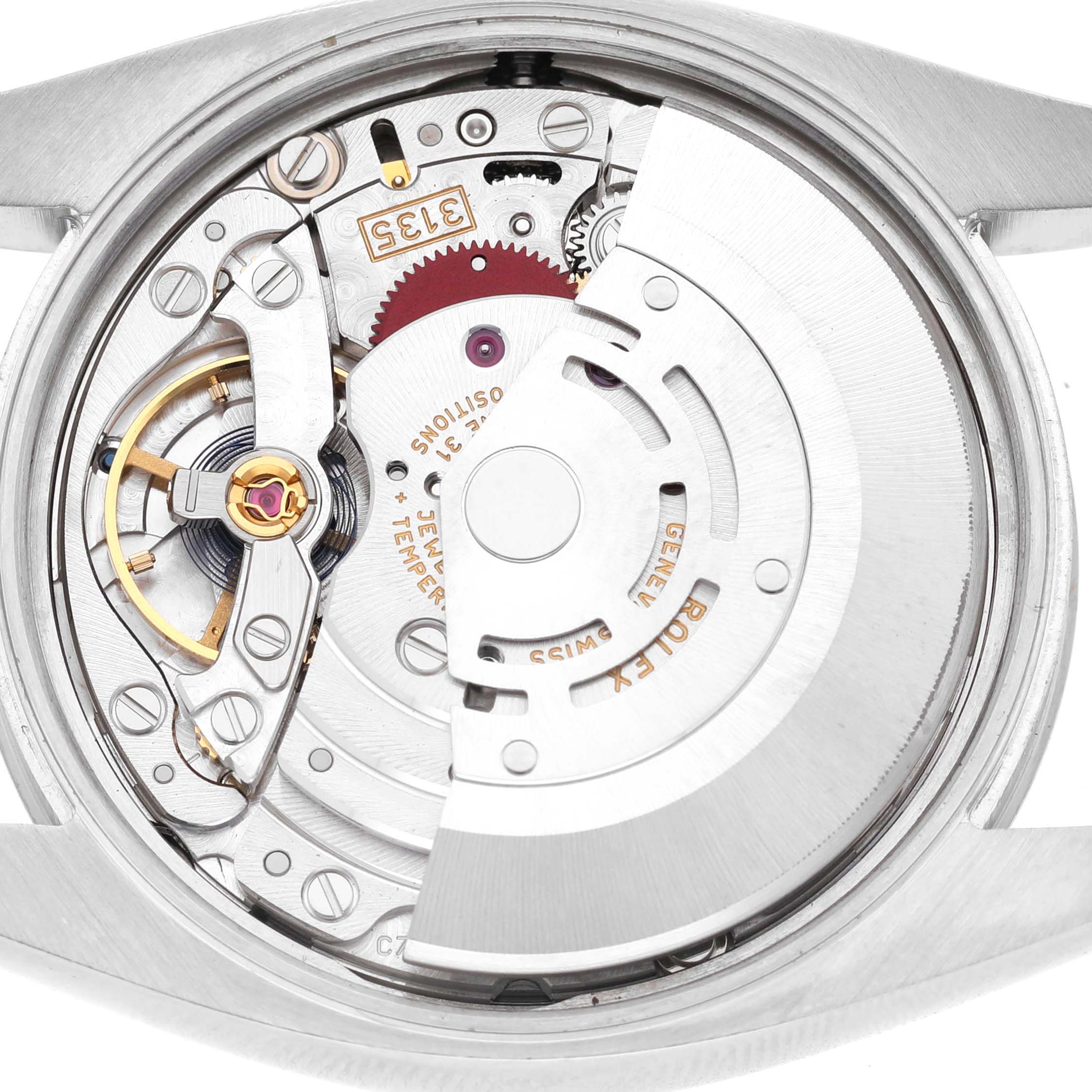 The image shows the movement of a Rolex Date 115234 Men's Stainless Steel Silver Dial watch, viewed from the back, highlighting gears and the rotor.