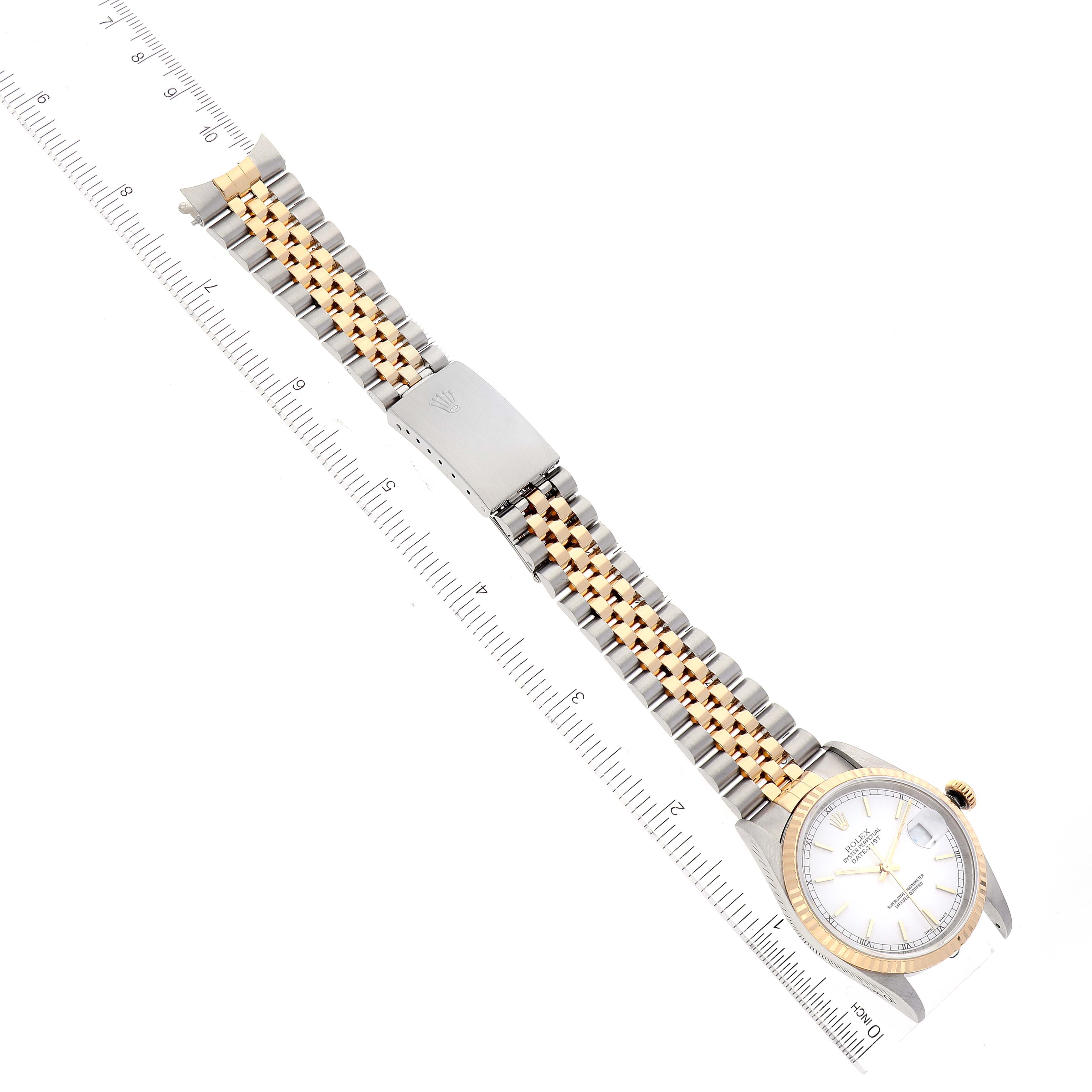 The Rolex Datejust 16233 Men's Steel and Gold (two tone) White Dial 16233 Men's Steel and Gold (two tone) White Dial watch is displayed laid flat, showcasing its face, bracelet, and clasp, alongside a ruler for size reference.