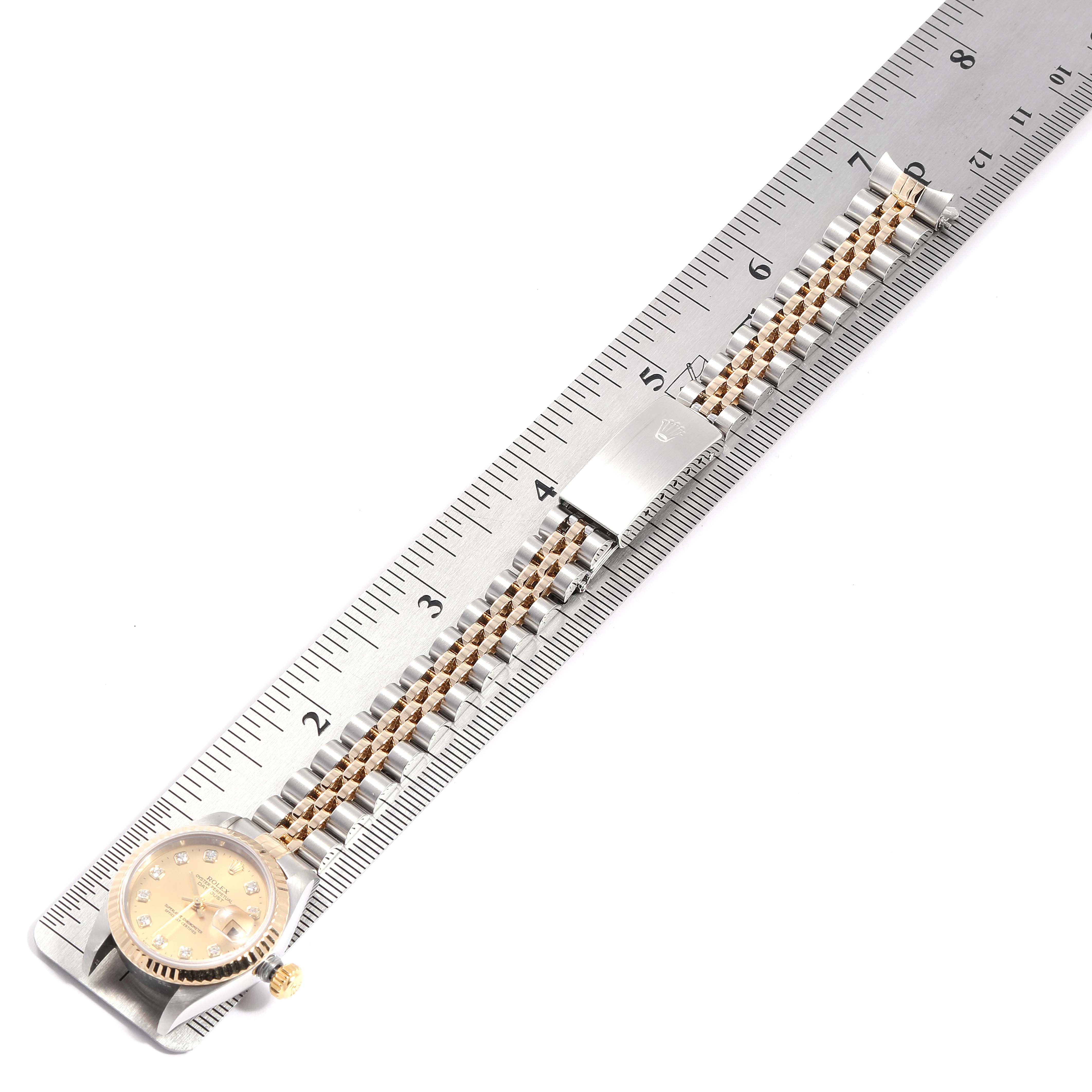The Rolex Datejust 79173 Women's Steel and Gold (two tone) Champagne Dial 79173 Women's Steel and Gold (two tone) Champagne Dial watch is shown from a top-down angle, focusing on the face, bracelet, and clasp, placed along a ruler.