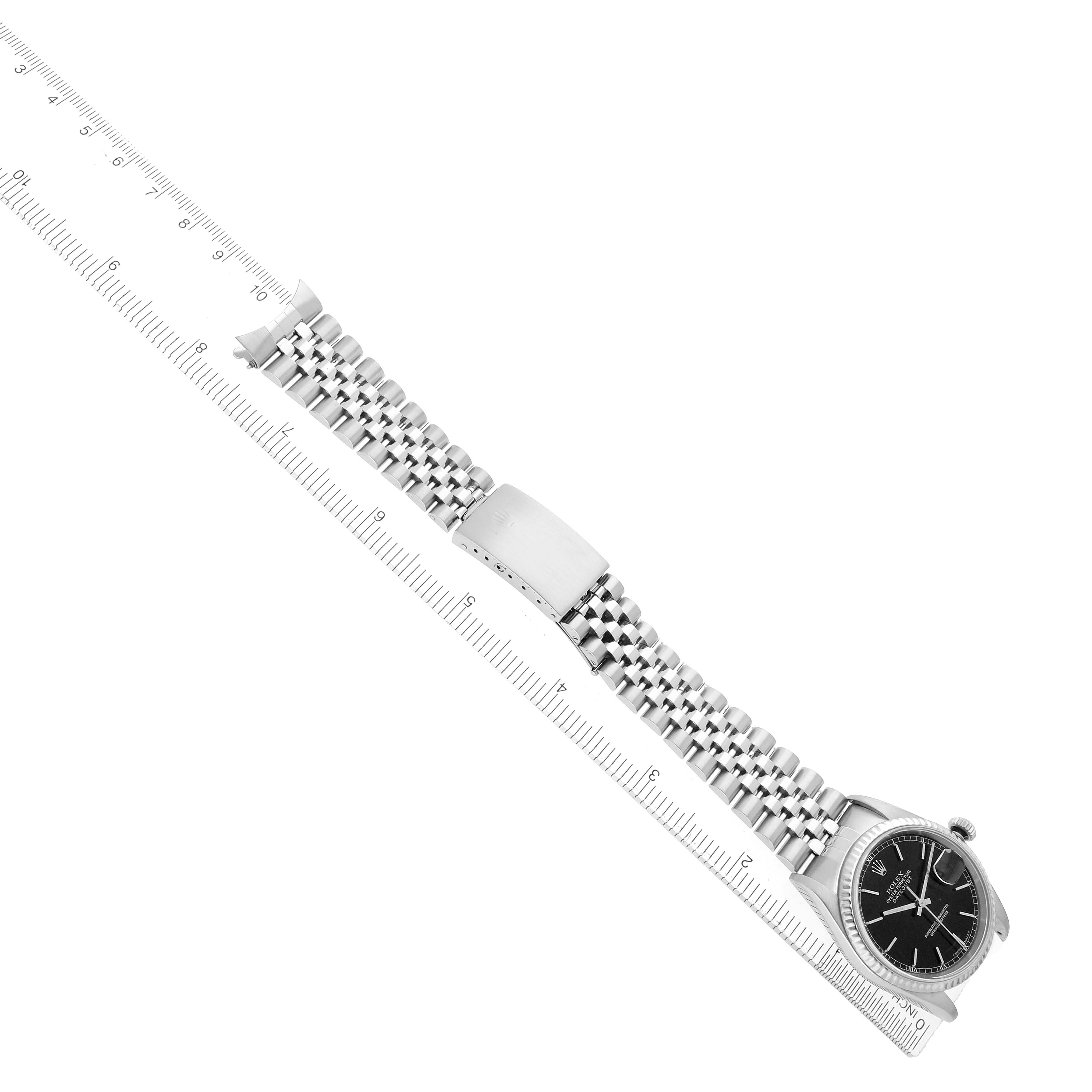 The image shows a Rolex Datejust 16234 Men
s Stainless Steel Black Dial watch laid flat, with a focus on the bracelet and clasp, beside a ruler for scale.