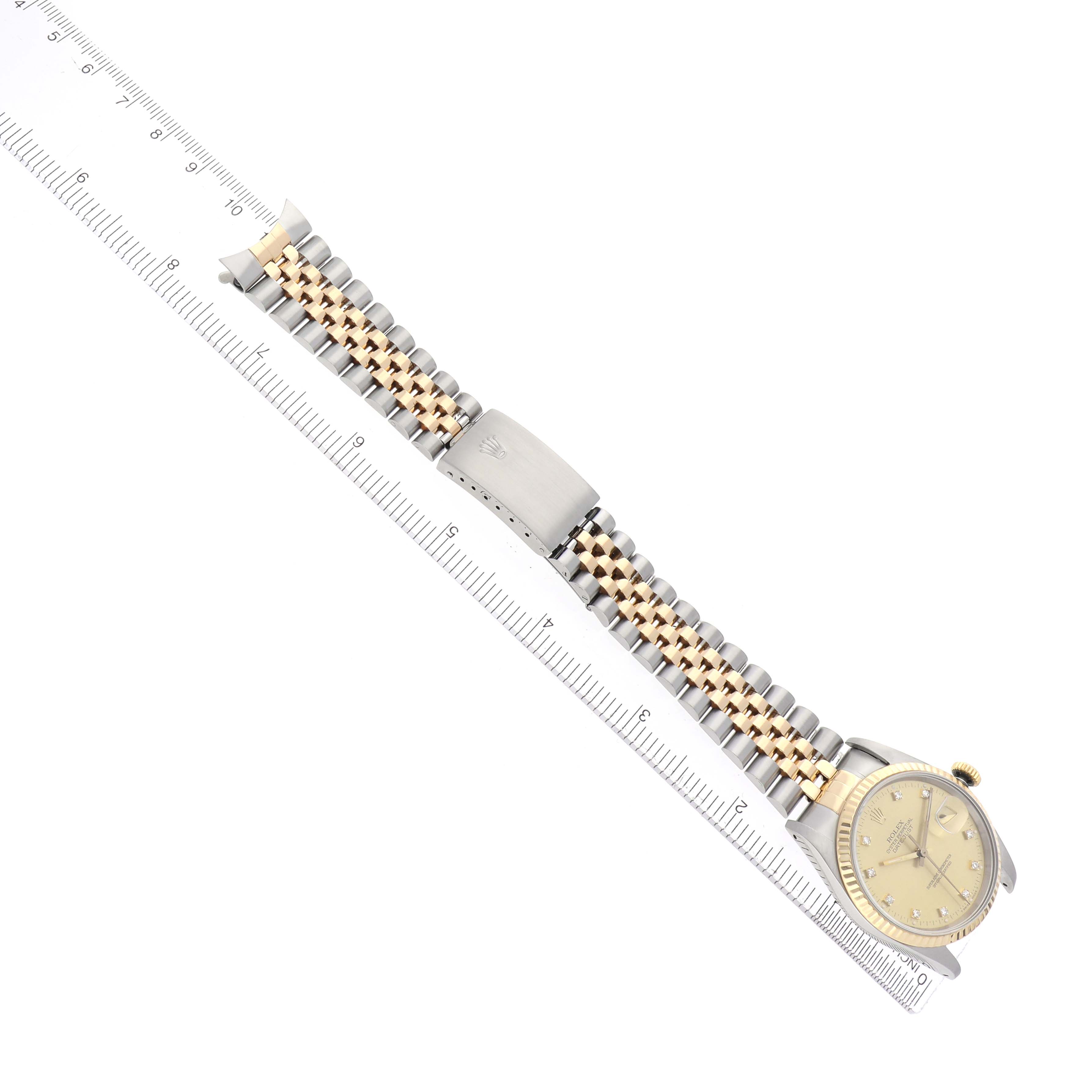 The Rolex Datejust 16233 Men
s Steel and Gold (two tone) Champagne Dial watch is shown at an angle displaying the face, bracelet, and clasp alongside a ruler for scale.