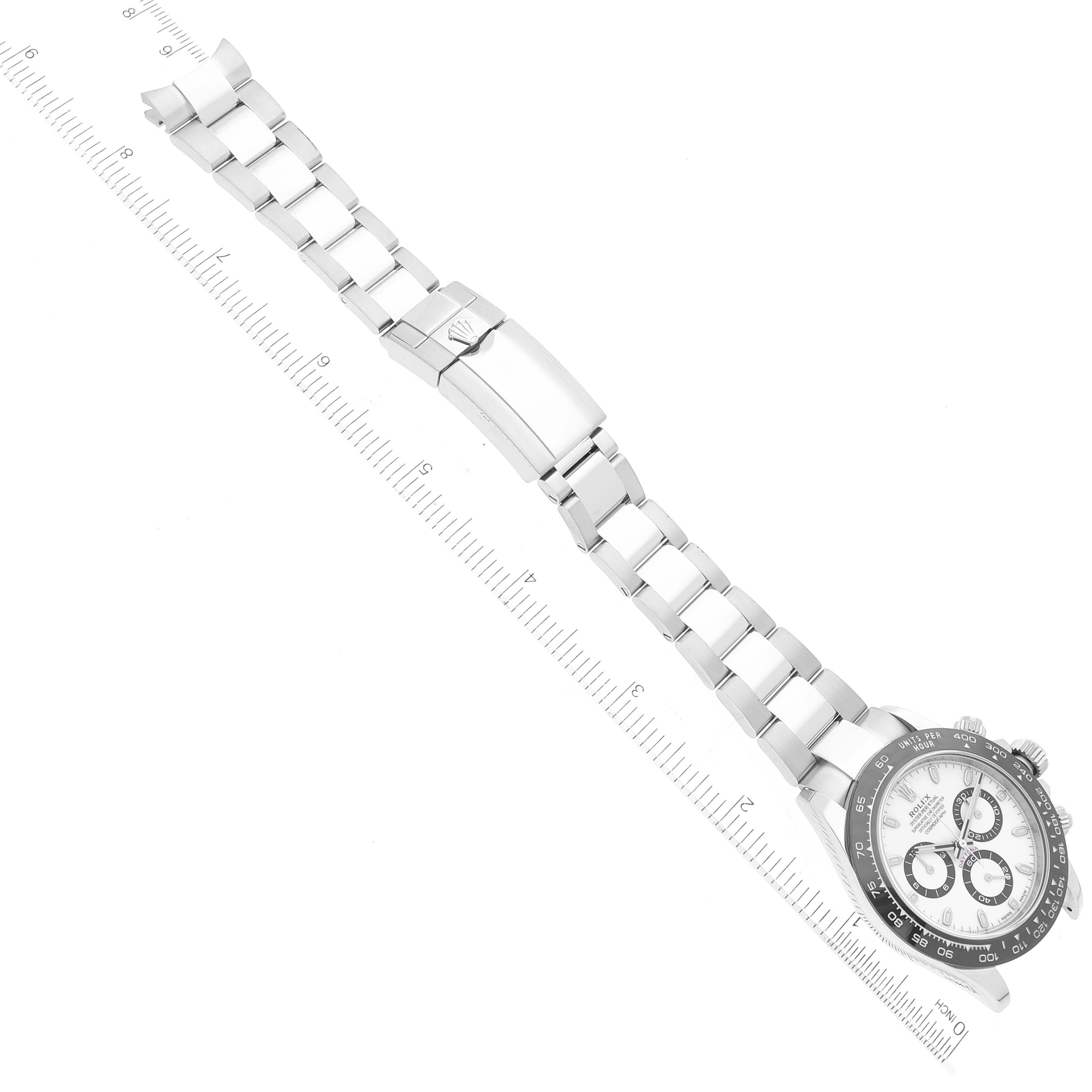 The image shows a top view of a Rolex Daytona 116500 Men
s Stainless Steel White Dial 116500 Men
s Stainless Steel White Dial watch, focusing on its bracelet and clasp, aligned with a ruler for scale.