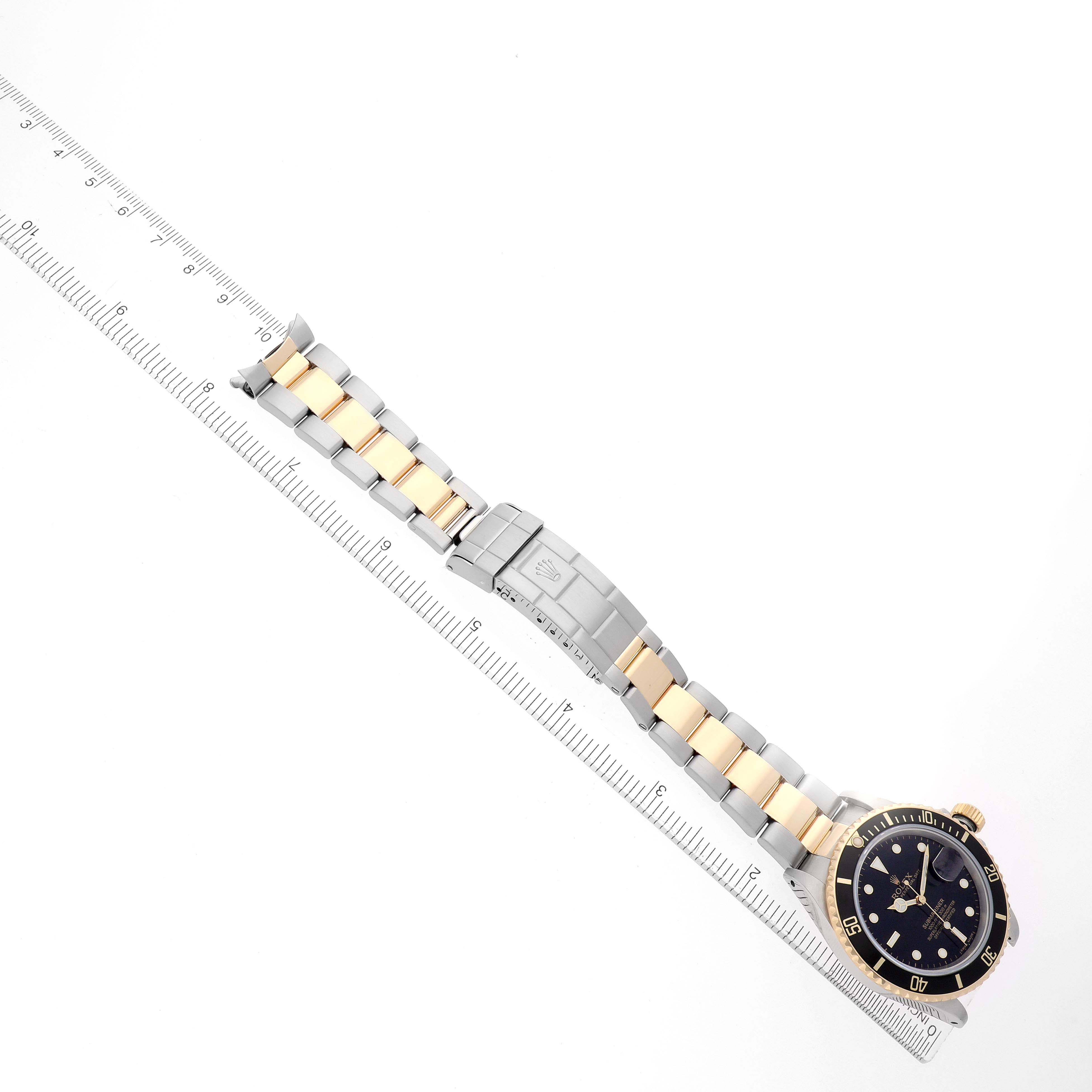 The Rolex Submariner 16803 Men
s Steel and Gold (two tone) Black Dial watch is shown at an overhead angle, highlighting the bracelet and clasp alongside a ruler.