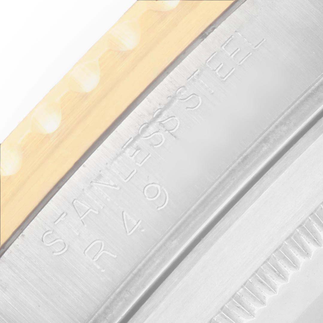 The image shows a close-up of the bezel and engraved edge of a Rolex Submariner 16803 Men
s Steel and Gold (two tone) Black Dial watch from the side angle.