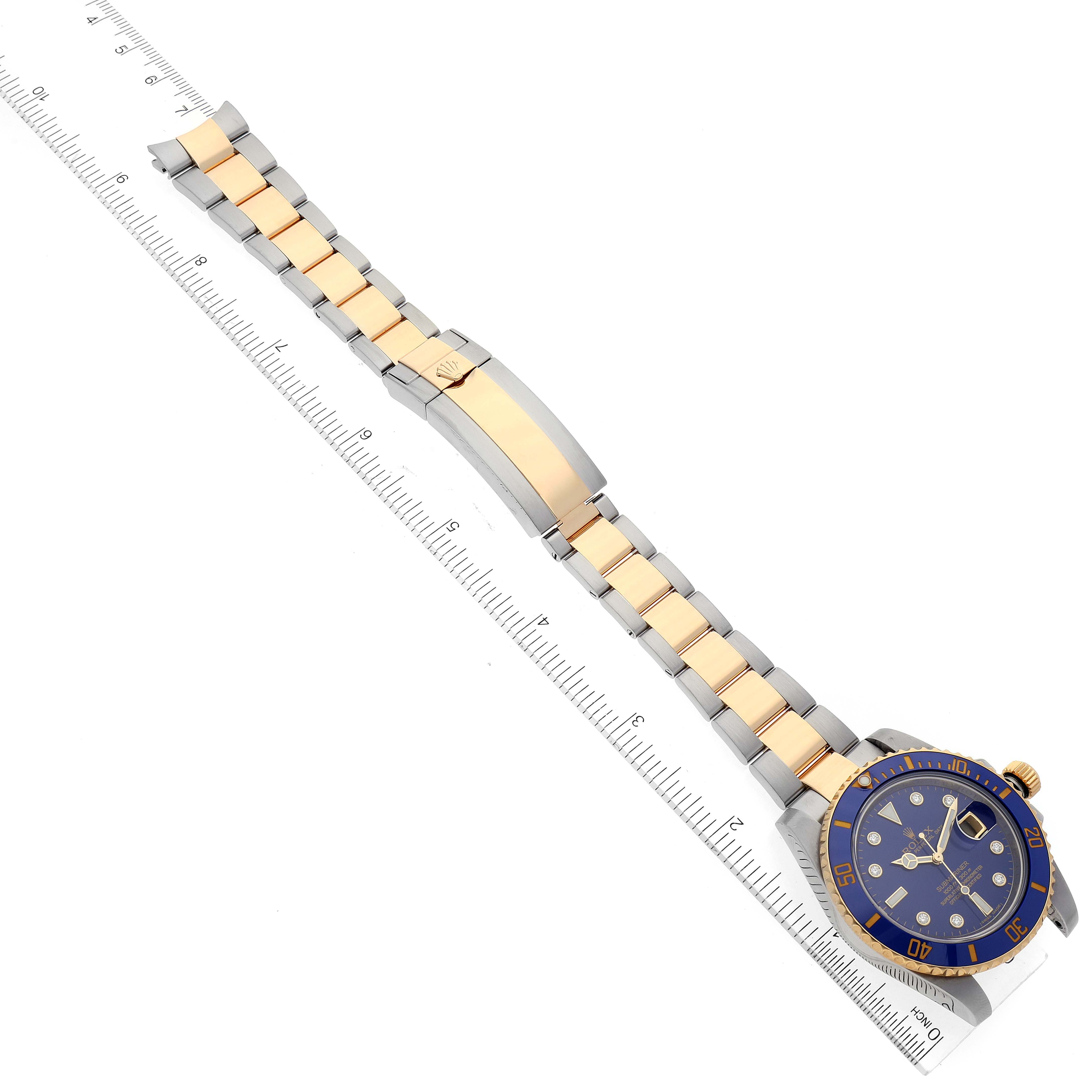 The image shows a top view of a Rolex Submariner 116613 Men's Steel and Gold (two tone) Blue Dial 116613 Men's Steel and Gold (two tone) Blue Dial watch, highlighting its band, clasp, and dial next to a ruler for scale.